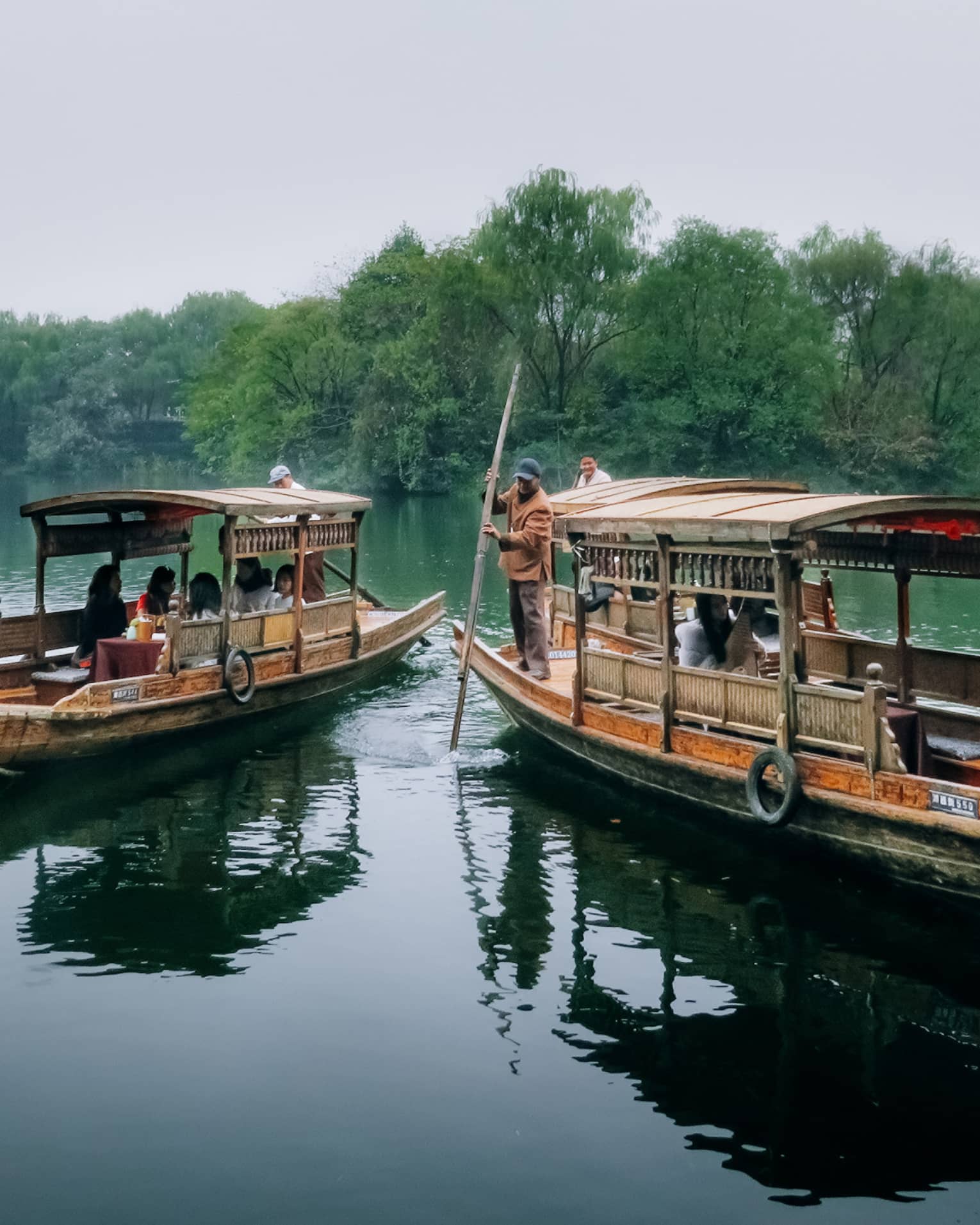 People dine on Chinese wooden rowboat next to boat where man steers with paddle on West Lake