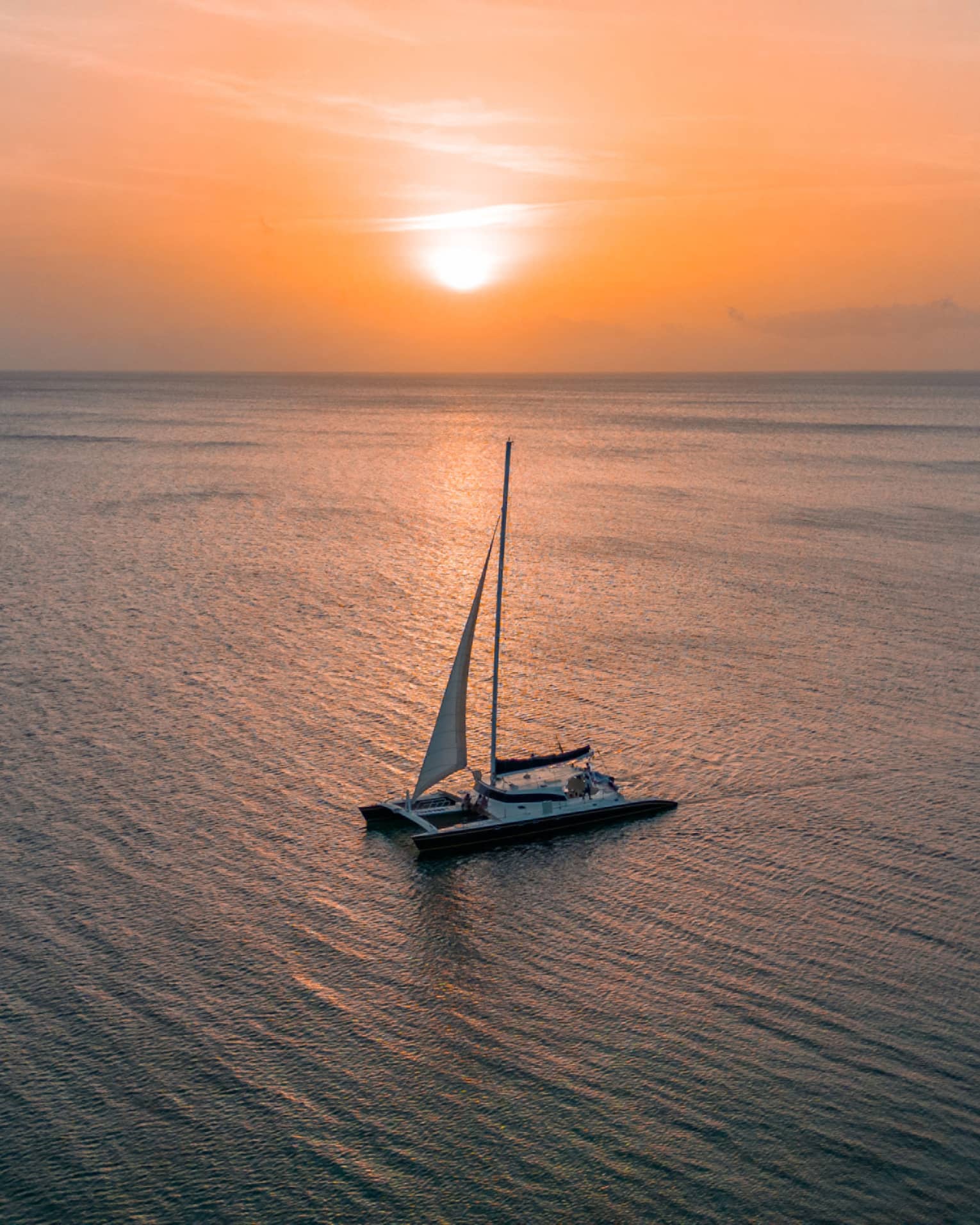 Aerial view of a sailboat floating through calm ocean waters at sunset