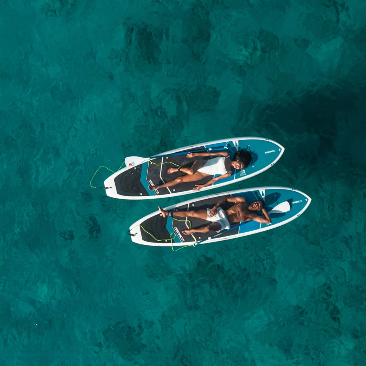 Two people lay on SUP paddleboards on the water