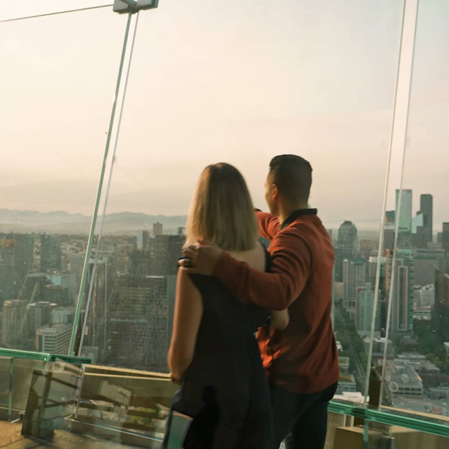 A man and woman walking in a tall building with glass walls looking out at a city.