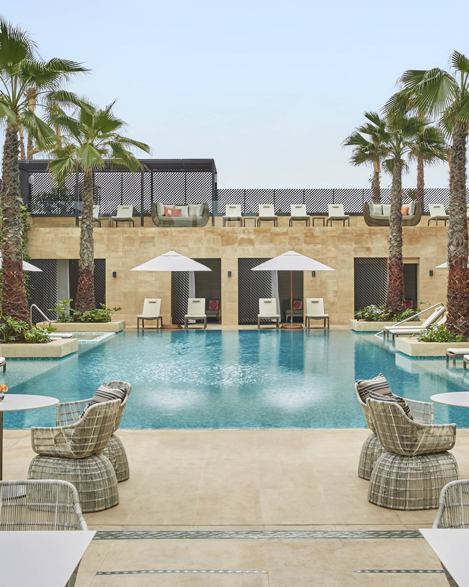 Courtyard pool flanked by tables and chairs with umbrellas, palm trees