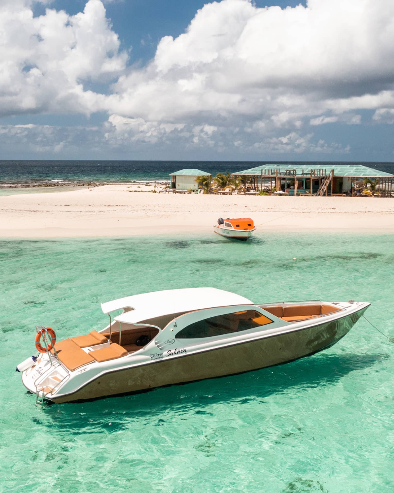 Luxury speedboat floating in clear turquoise water near a sandy island with a beach hut.