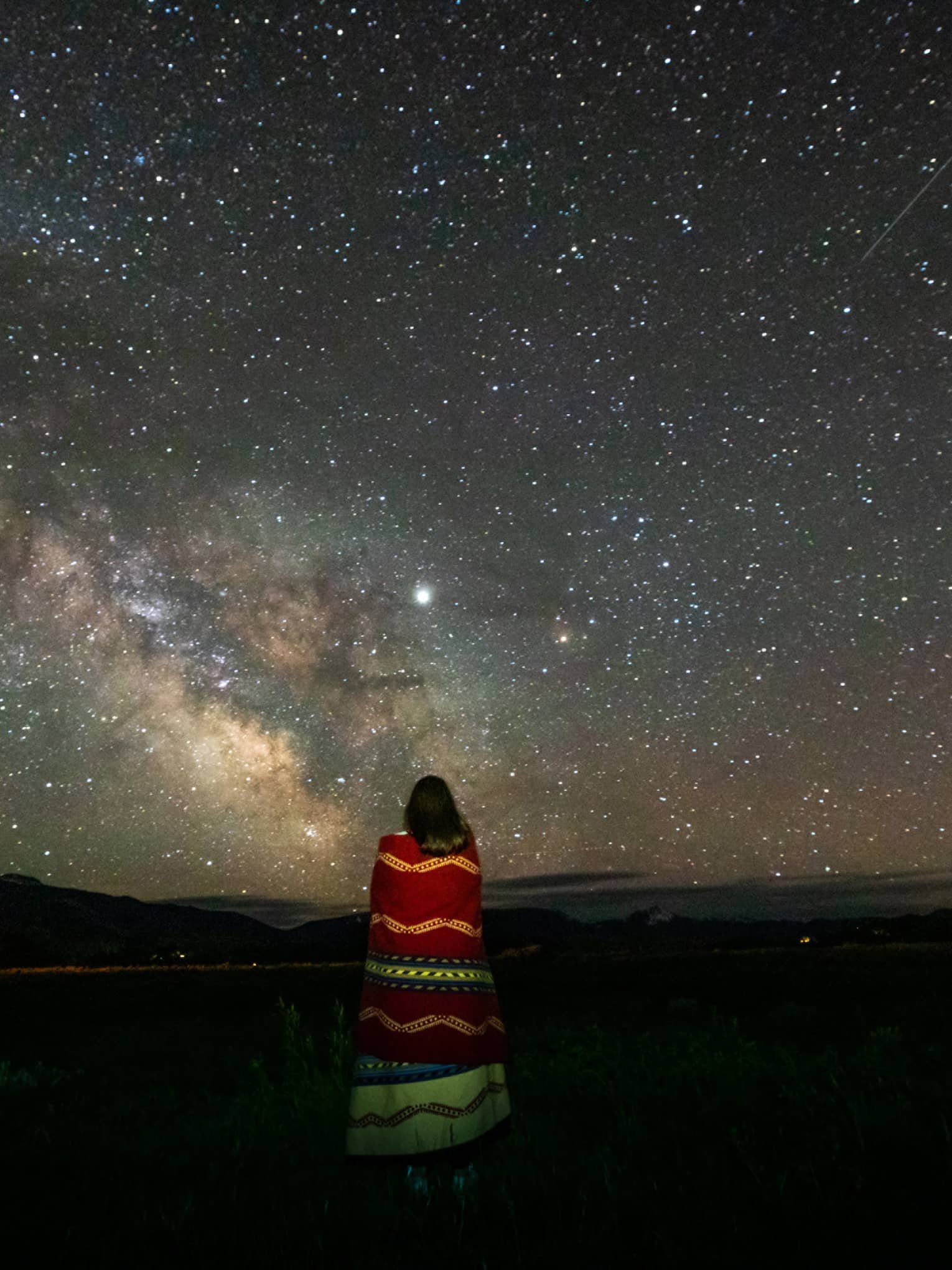 A lone woman stargazes, wrapped in a colourful striped blanket 