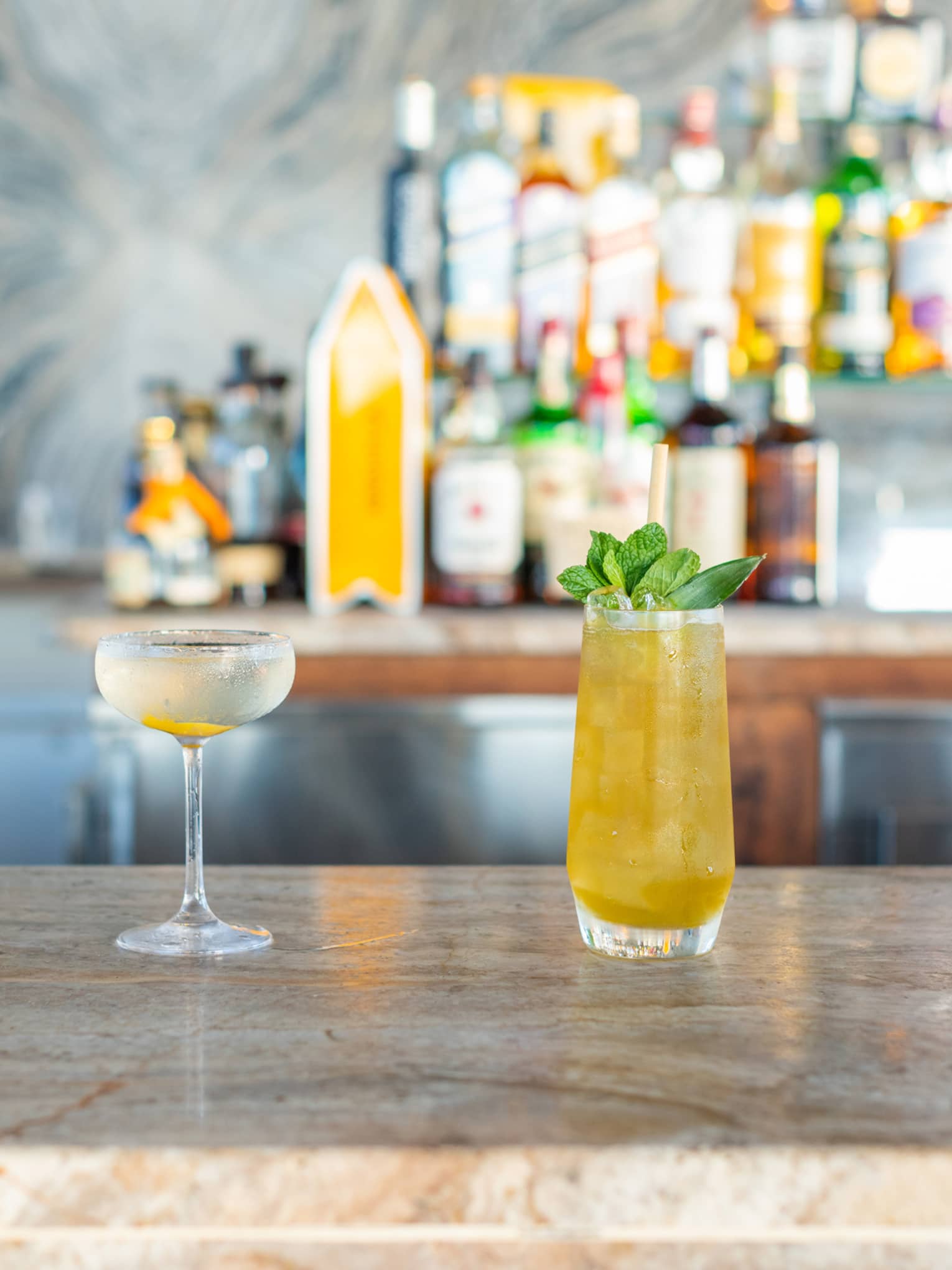 Four cocktails on a bar counter with bottles behind them.