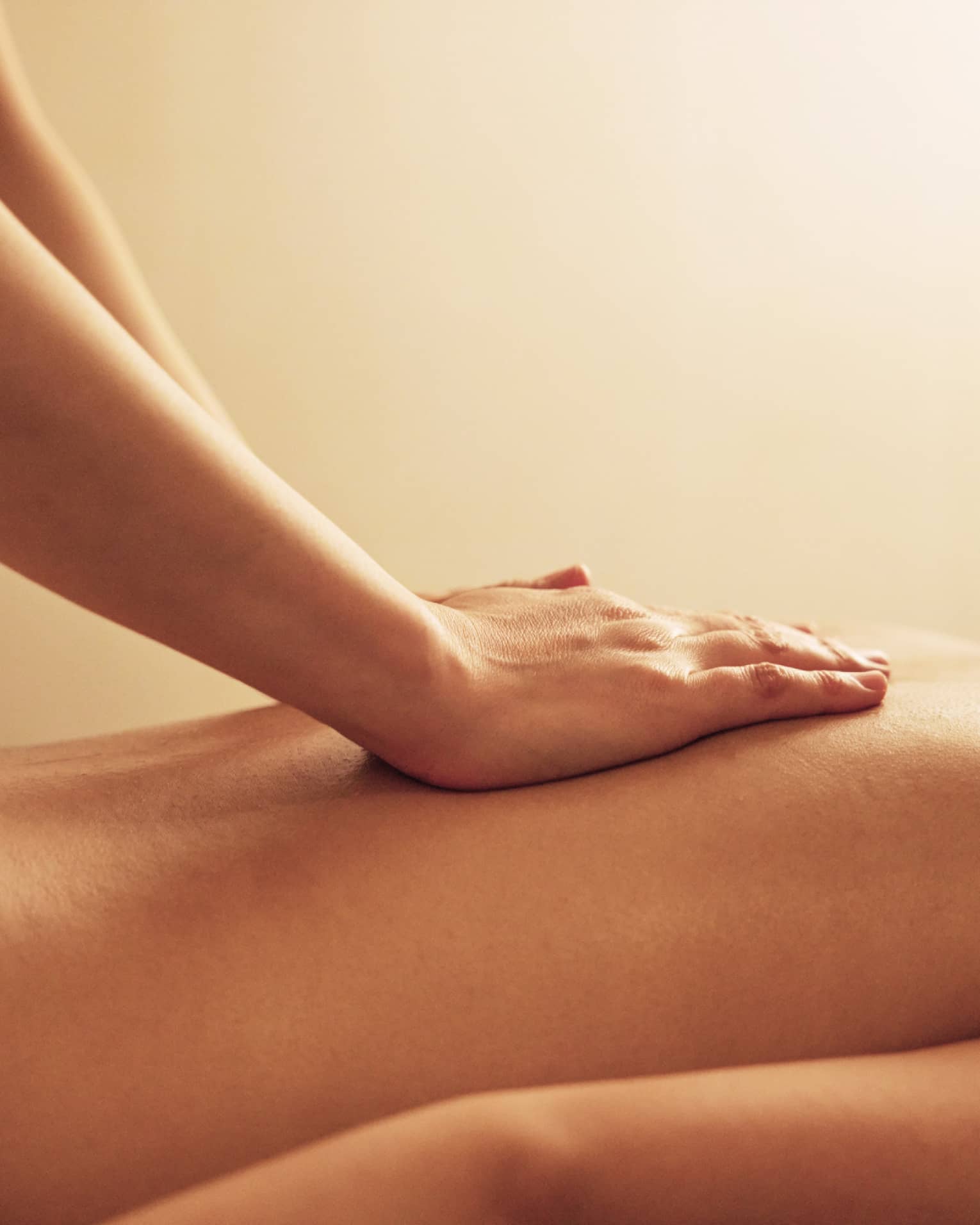 Masseuse rests hands on woman's bare back as she lays on massage table