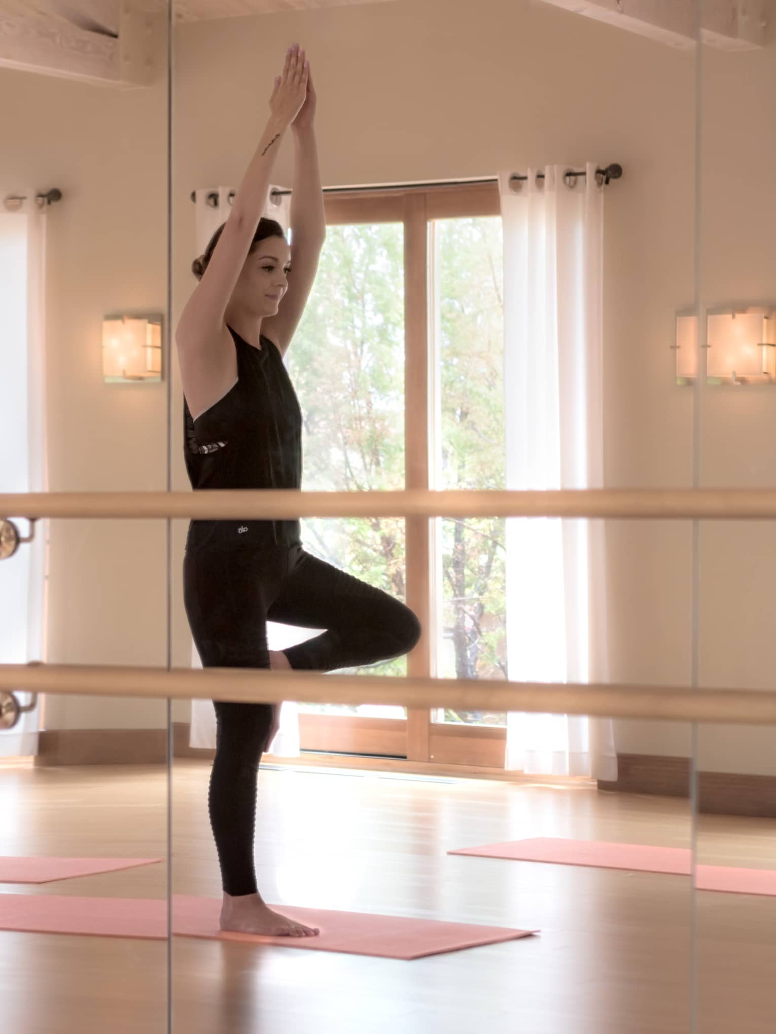 Mirror reflection of three people standing in yoga pose on mats in fitness centre