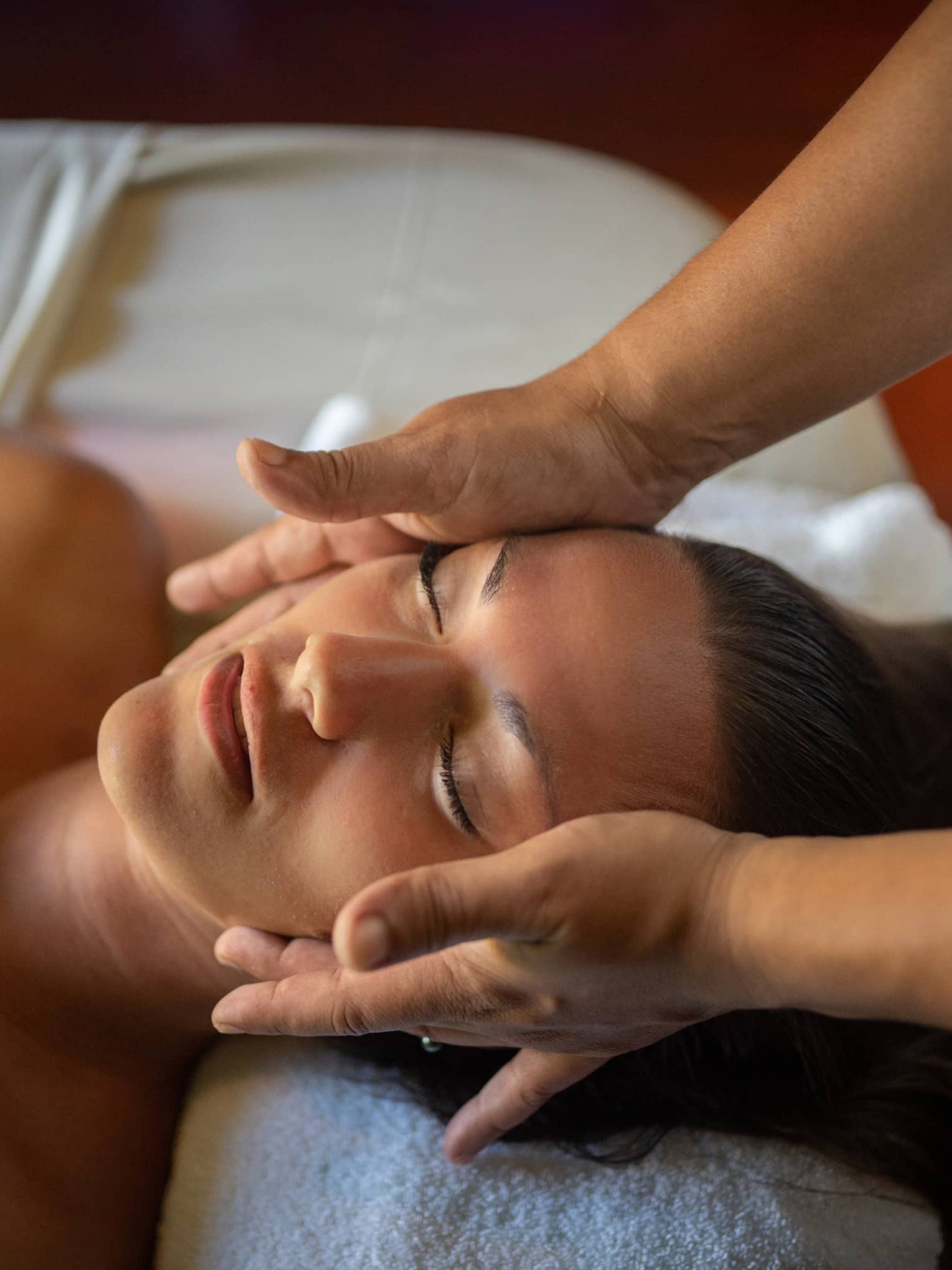 Woman lays on massage table with eyes closed as hands massage her cheeks and chin
