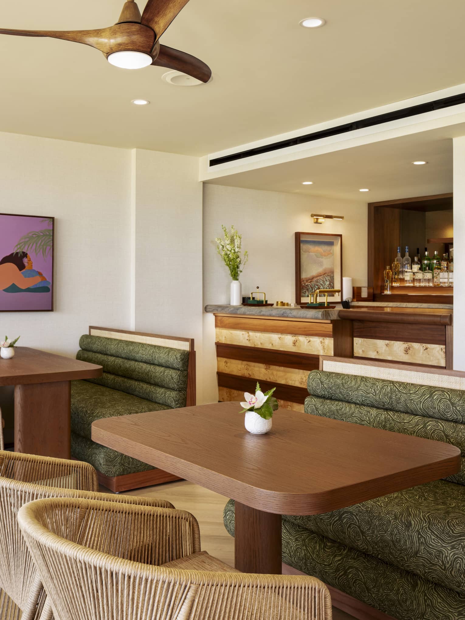 Wooden dining tables in an executive club lounge, featuring large green booths and woven beige chairs