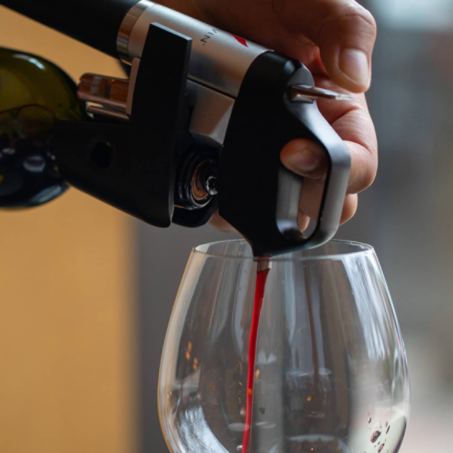 Their hands holding the bottle steady, a person pours scarlet red wine through an aerator device into a glass.