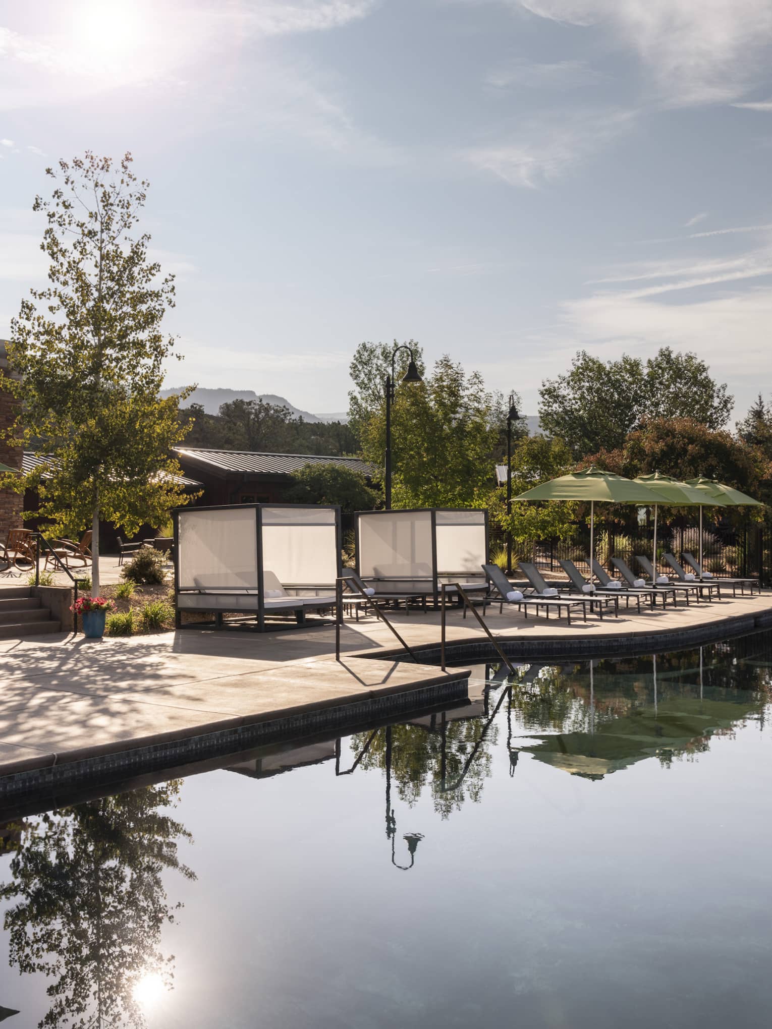 An outdoor pool with lounge chairs and green umbrellas near it.