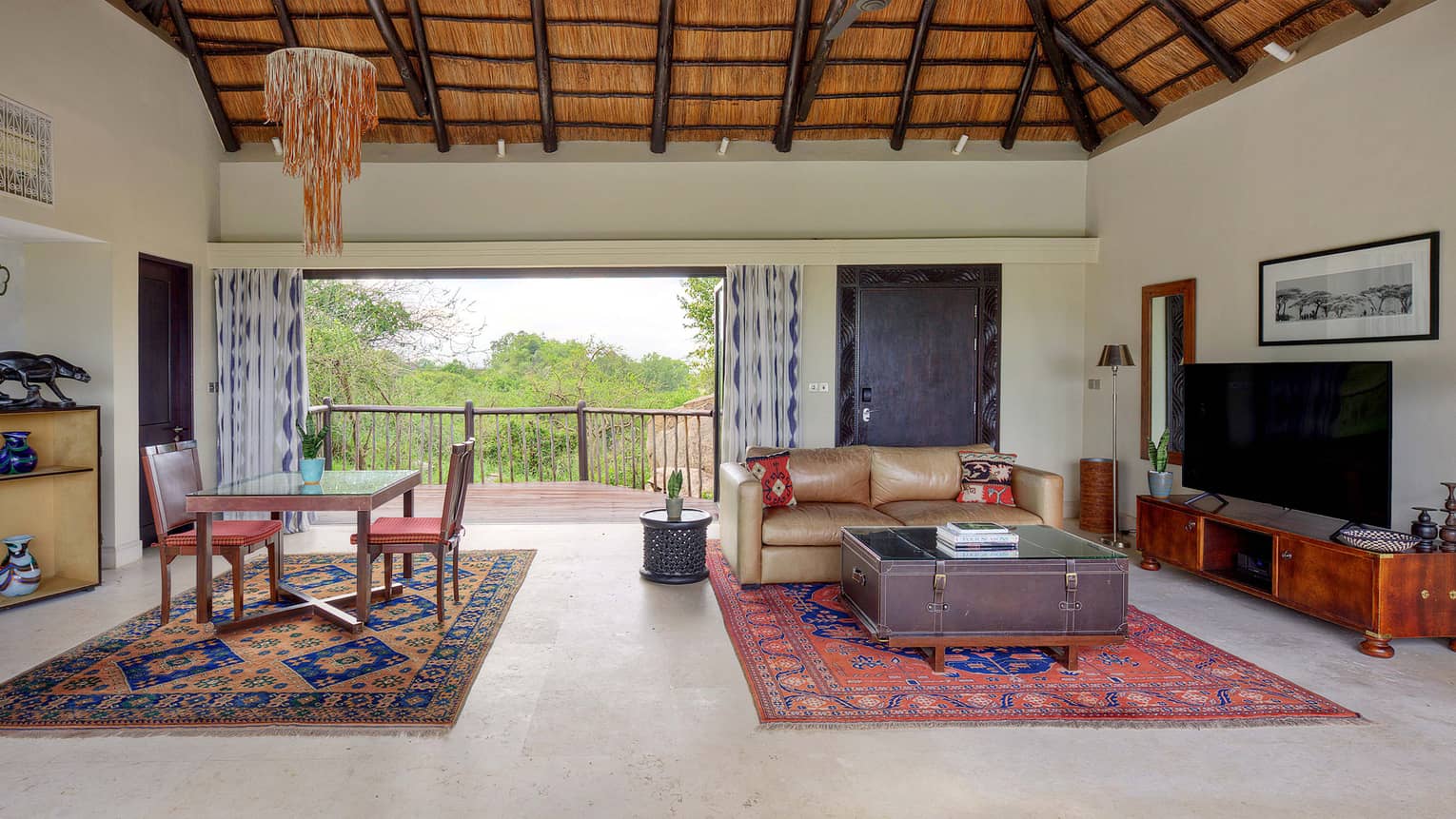 Large villa with two ethnically inspired rugs, one with dining set and one with seating vignette, and a large-screen TV atop console