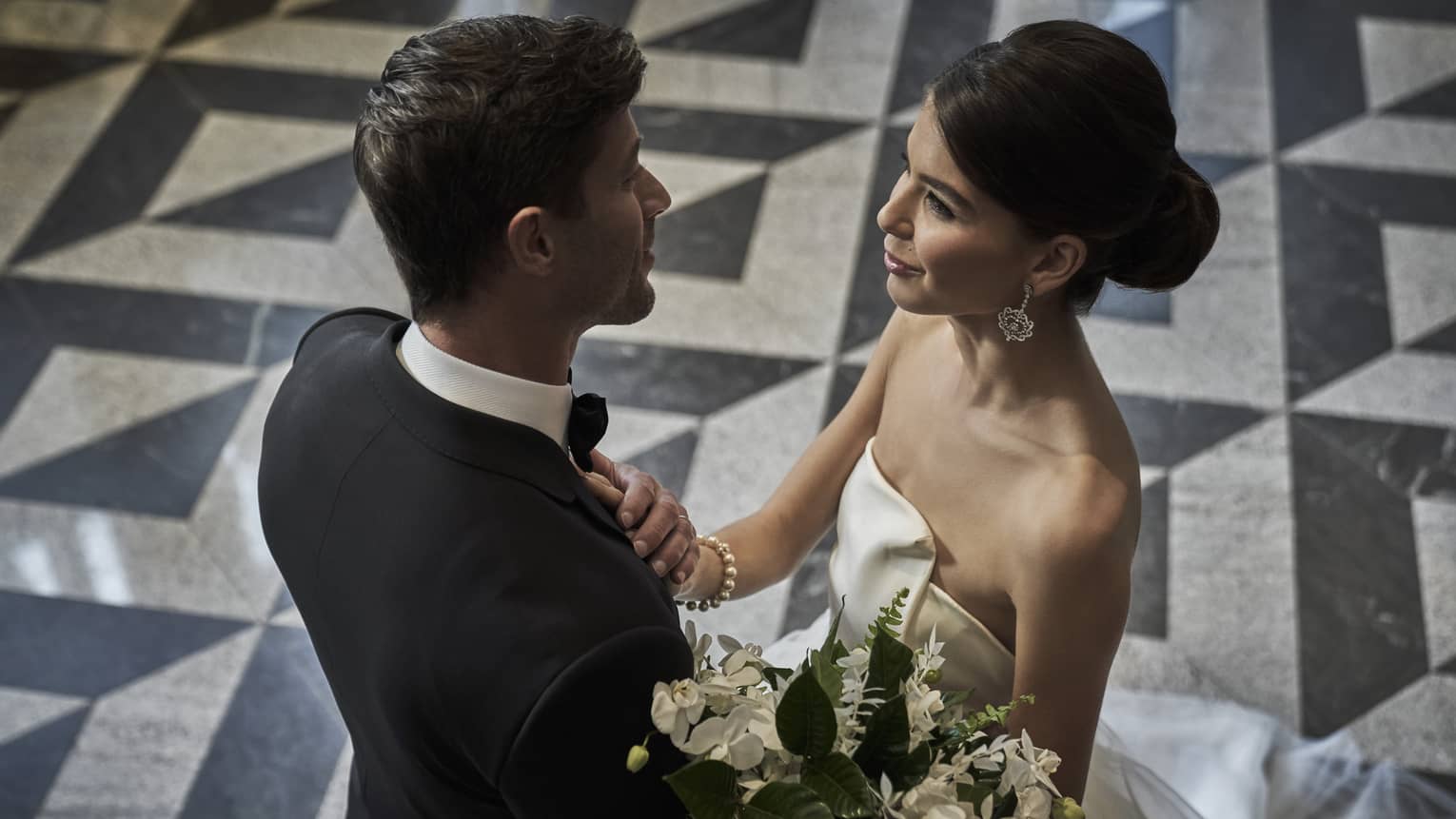 Groom and bride with white floral bouquet embrace in banquet room with black and white floors