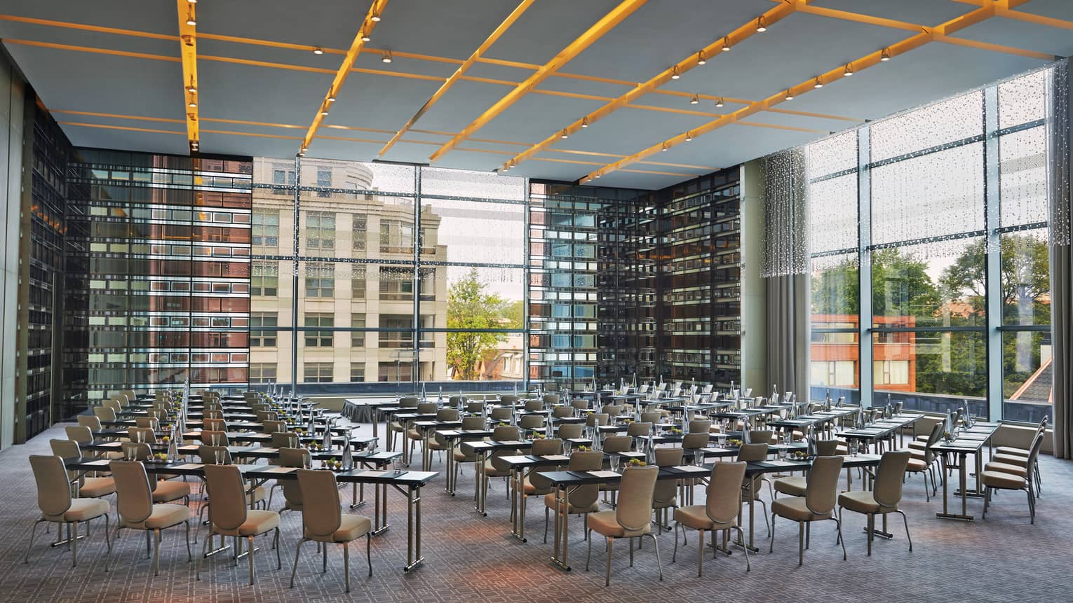 Chairs, tables set up in rows in glass room with corner windows 