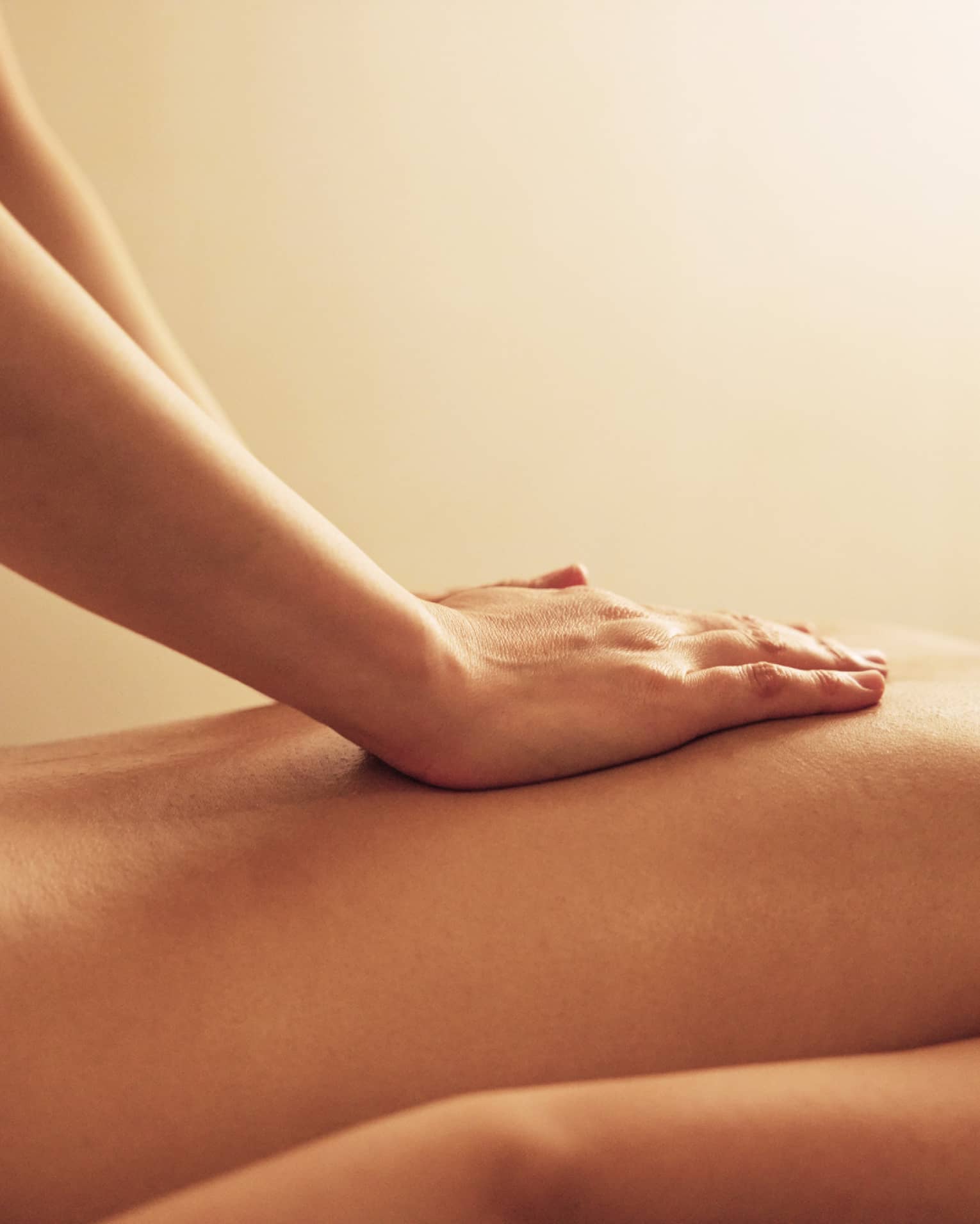 Masseuse rests hands on woman's bare back as she lays on massage table