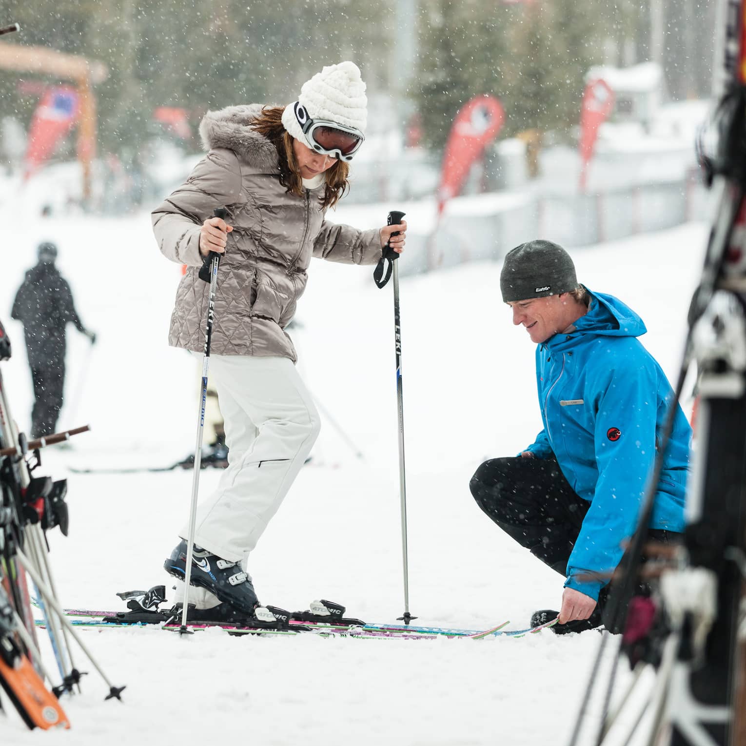 Ski concierge kneels down by woman trying on skis in front of rack