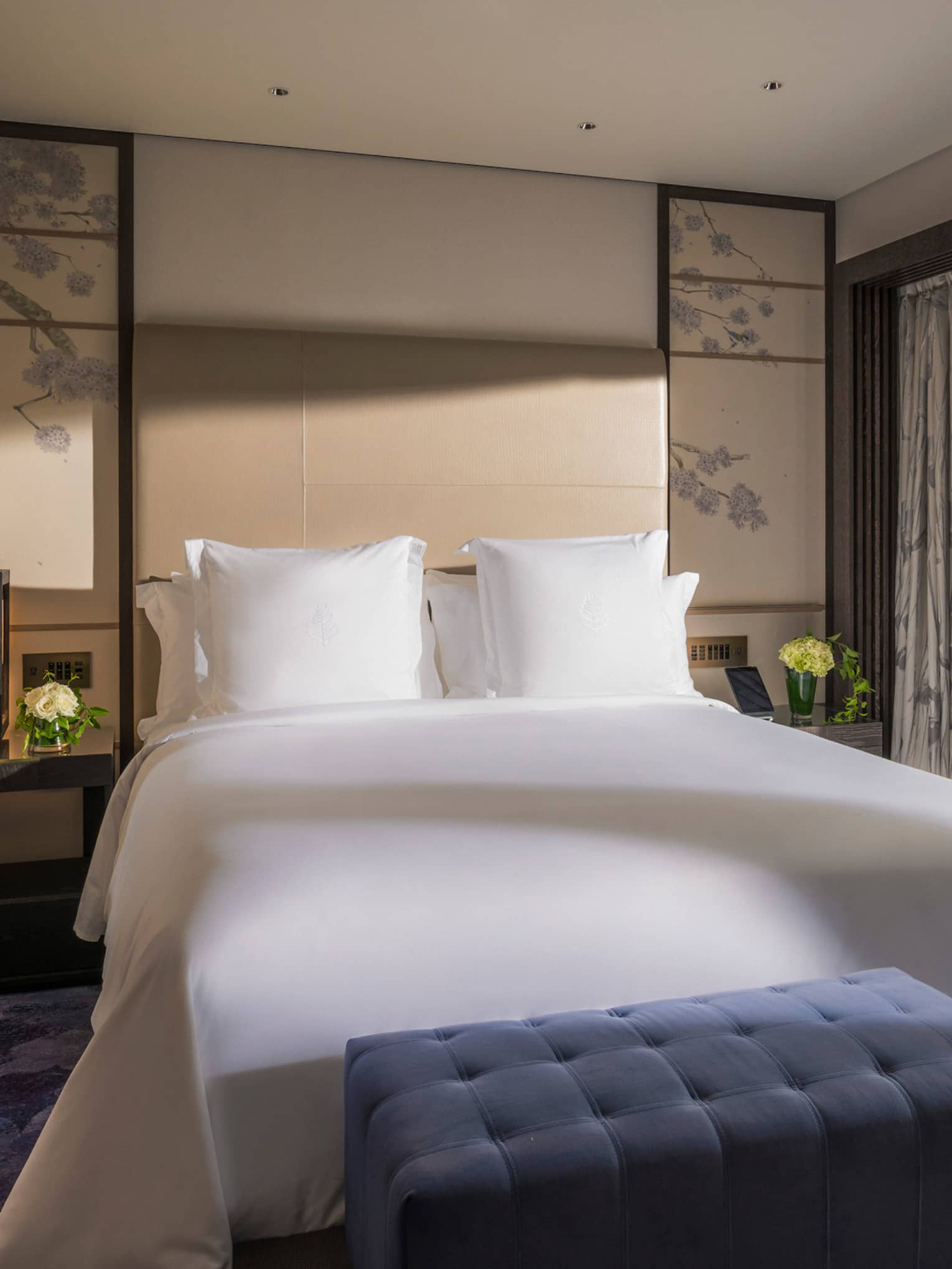 Bright bedroom with a king-size bed, a blue tufted bench and sliding glass doors opening to a private terrace with garden view