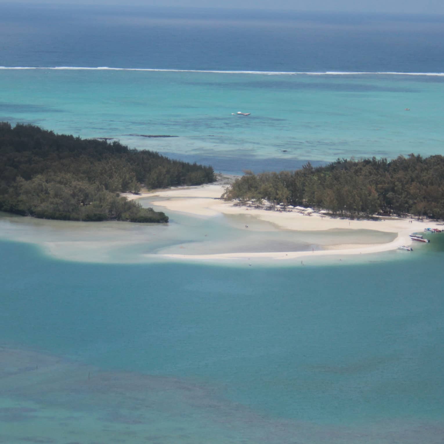 Two islands covered in lush forest separated by a white sandy beach, calm turquoise water receding toward a clear blue sky.