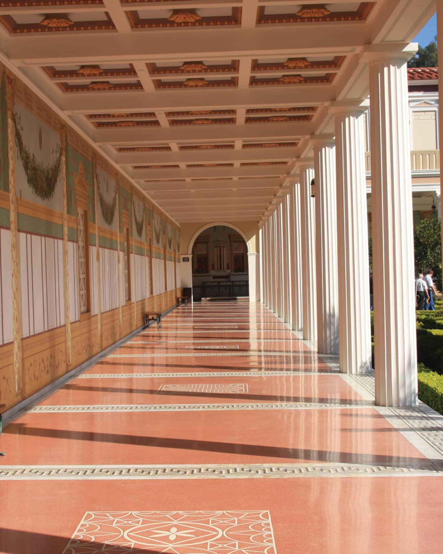 A long hallway with orange floors and columns on the side leading to an arched doorway.