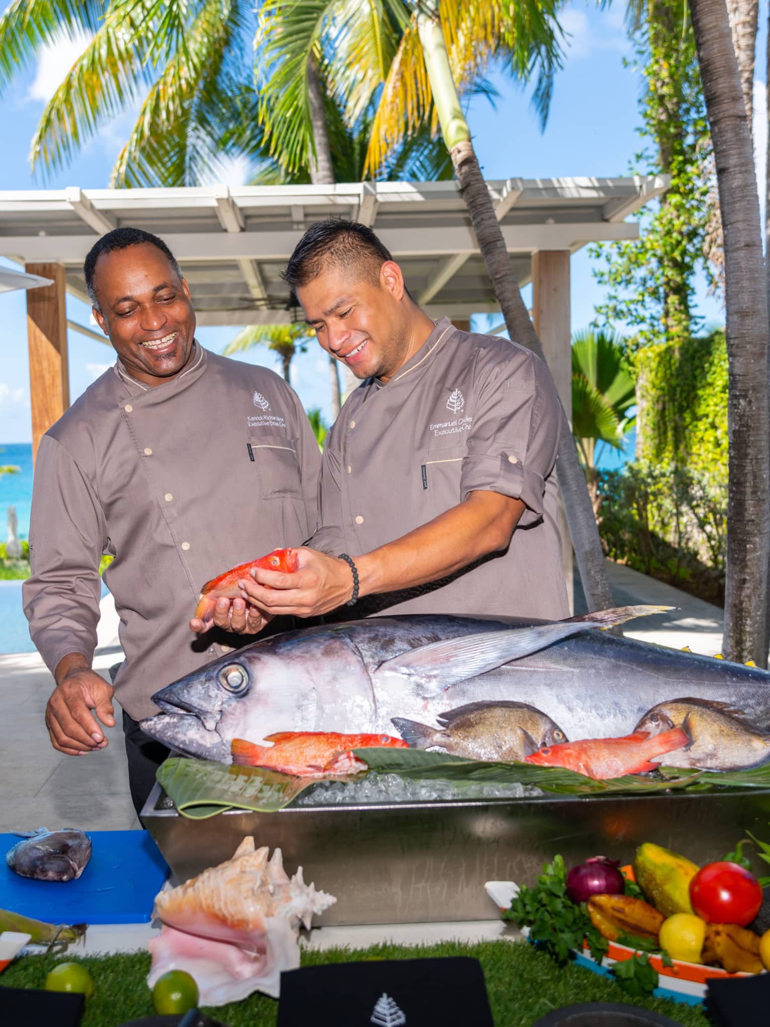 Two people standing in front of a food display with a large fish while holding a smaller fish.