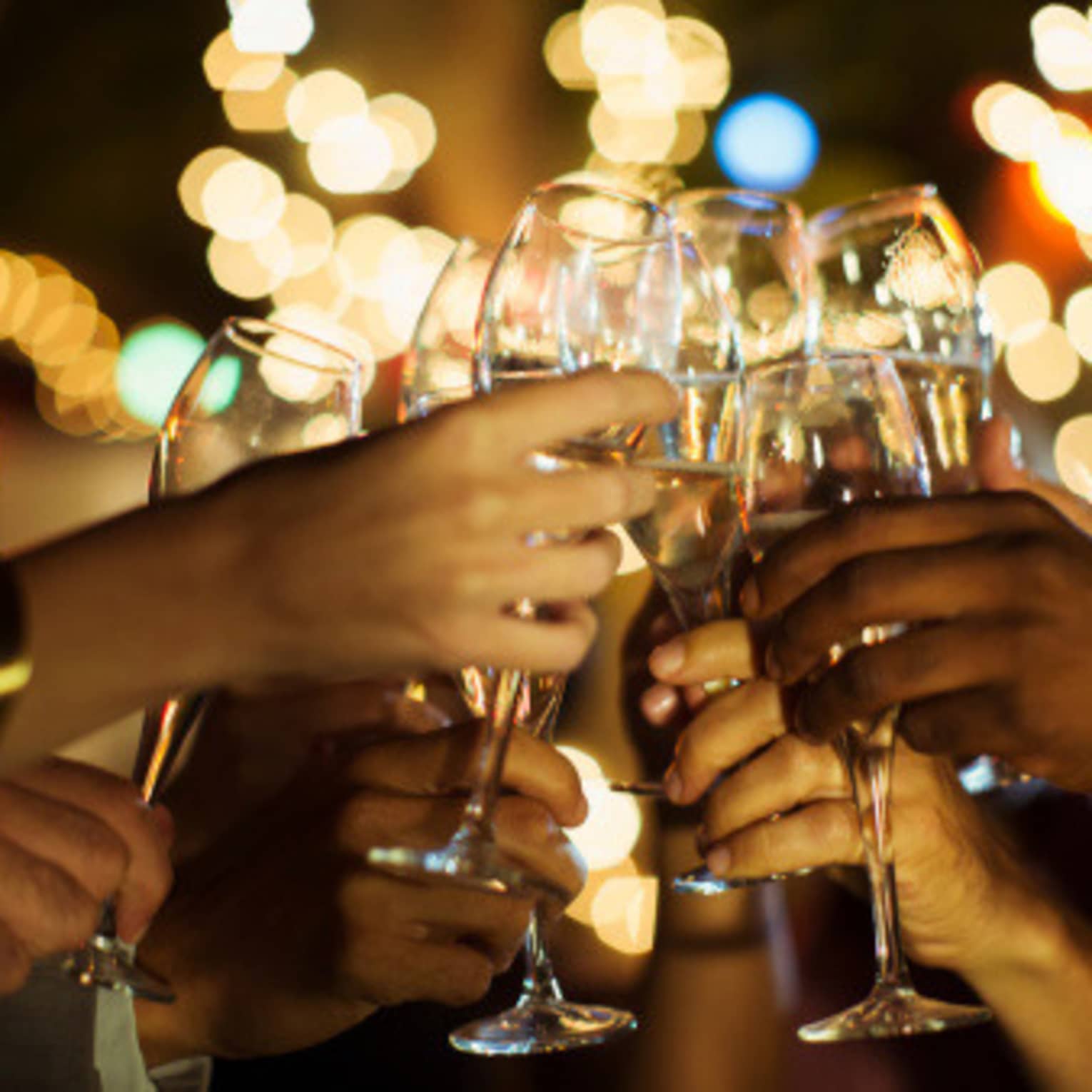 A group of guests clink their glasses of champagne together on a patio with twinkle lights
