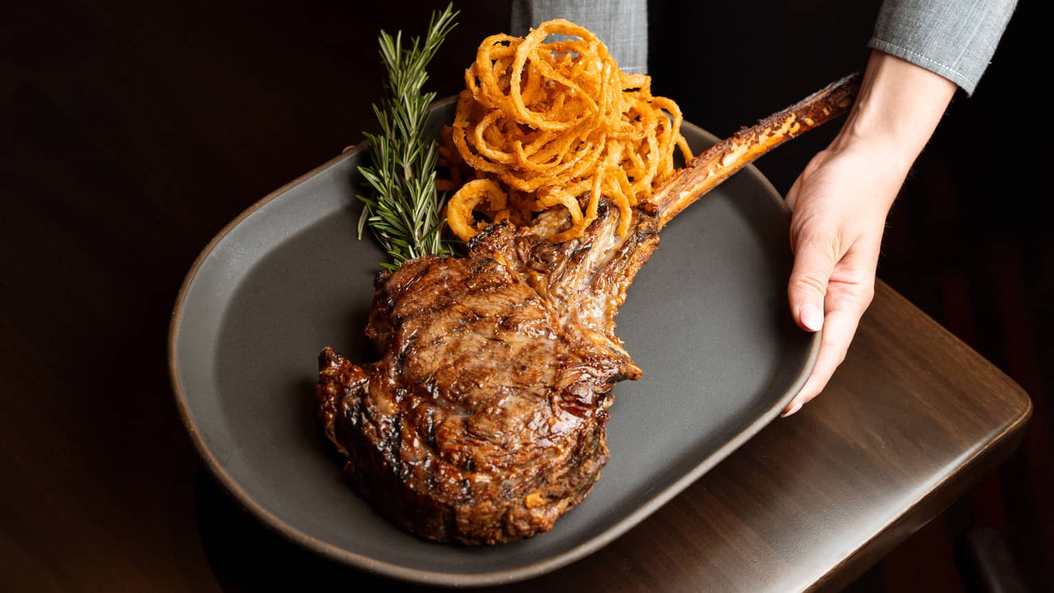 A person serving a large steak and onion rings on a plate
