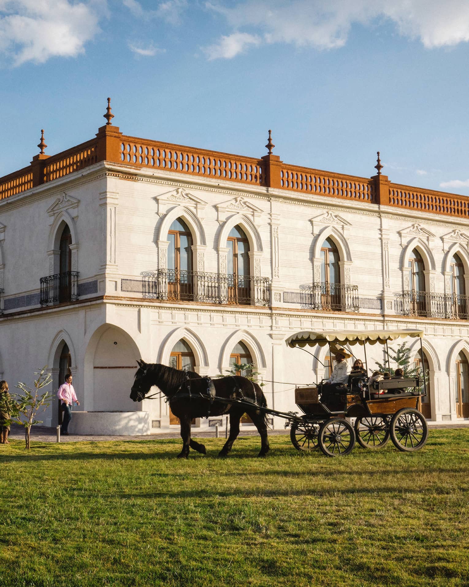 Guests enjoying a horse-drawn carriage ride around a large white building with several beautifully carved arched doorframes.