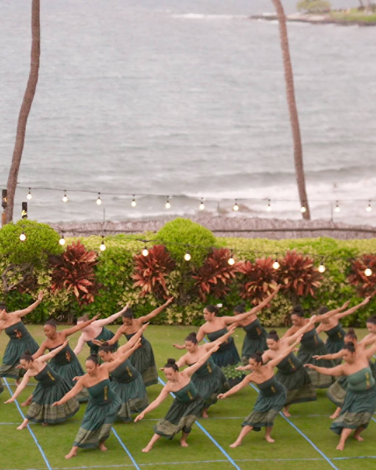 A group of hula dancers perform on an oceanside lawn at luxury resort