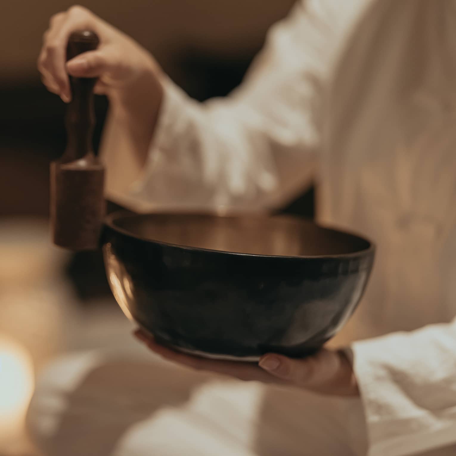 Close-up of an instructor rubbing a mallet against the edge of a sound bowl in a dimly lit room surround by burning candles.