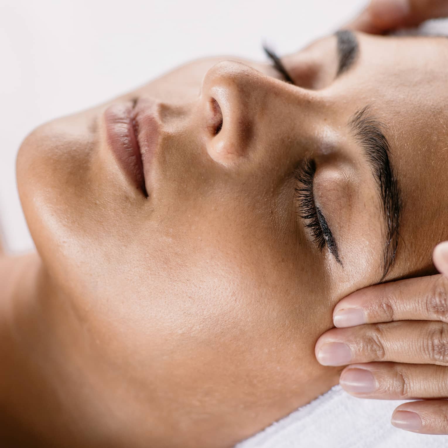 Hands massage woman's temples as she closes her eyes, spa towel around hair