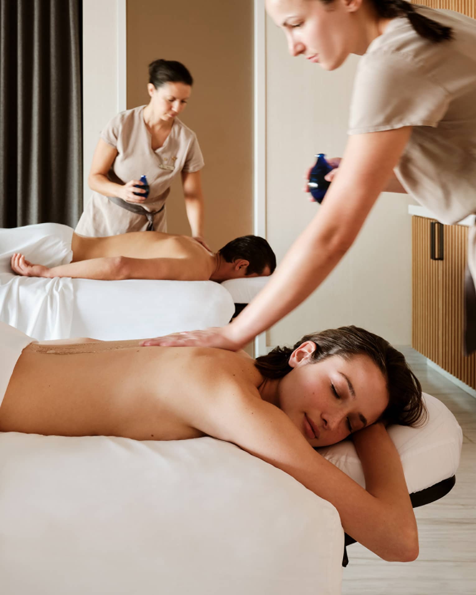 Couple lying prone on spa tables while being massage by spa therapists