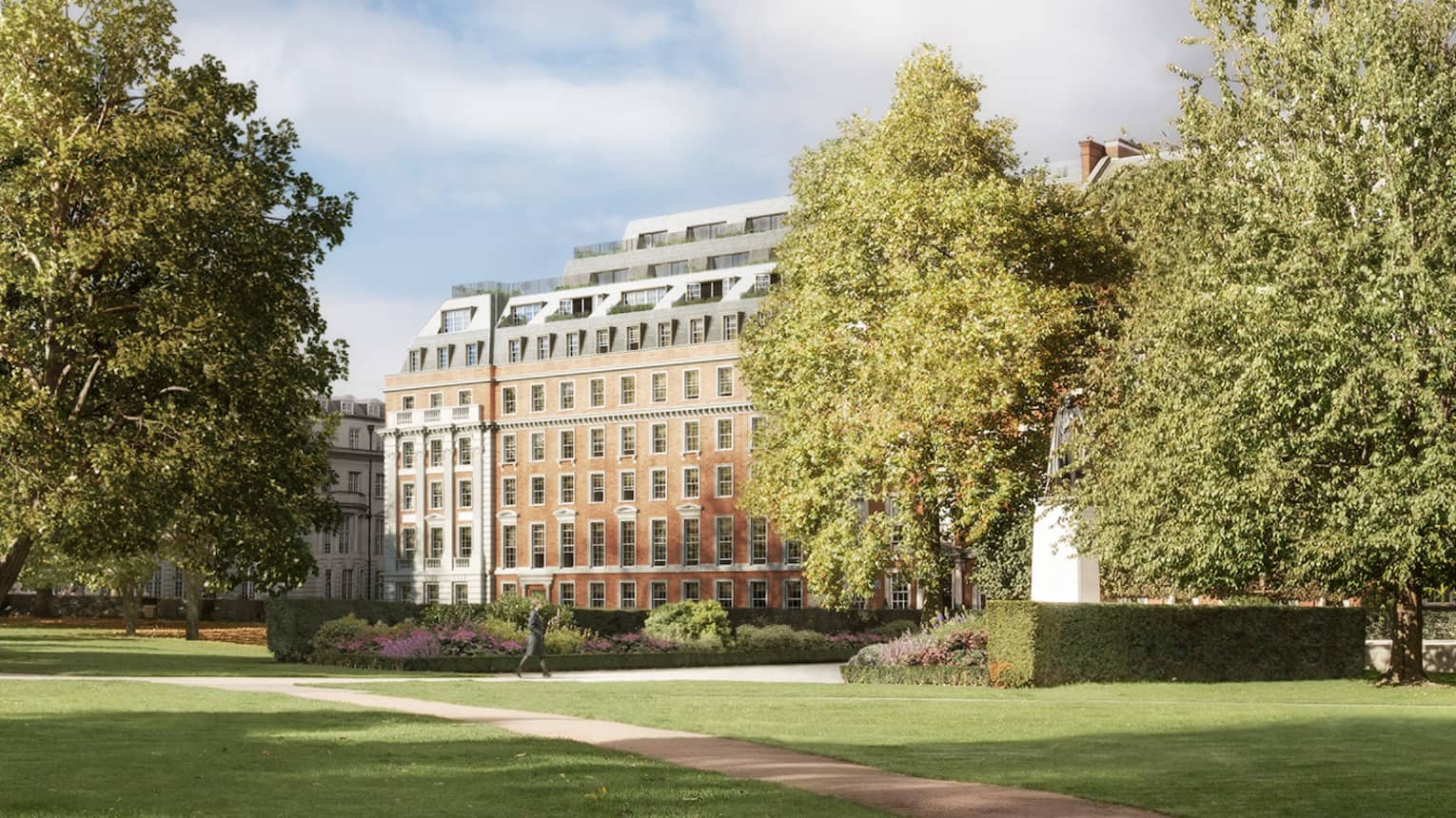 View across long green park, path between trees to building in background