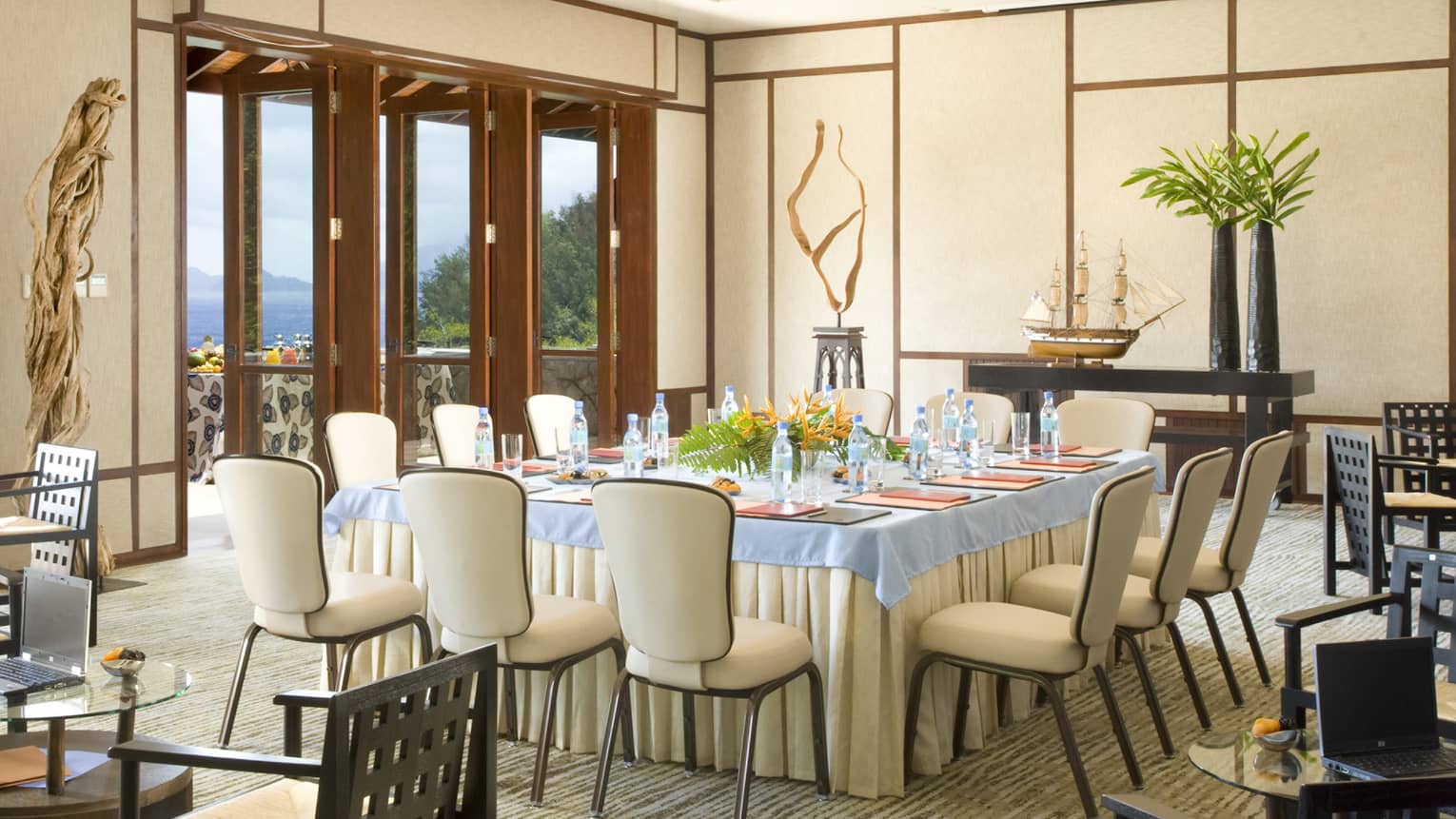 Light-filled conference room with square table with flowers, cream chairs overlooking ocean