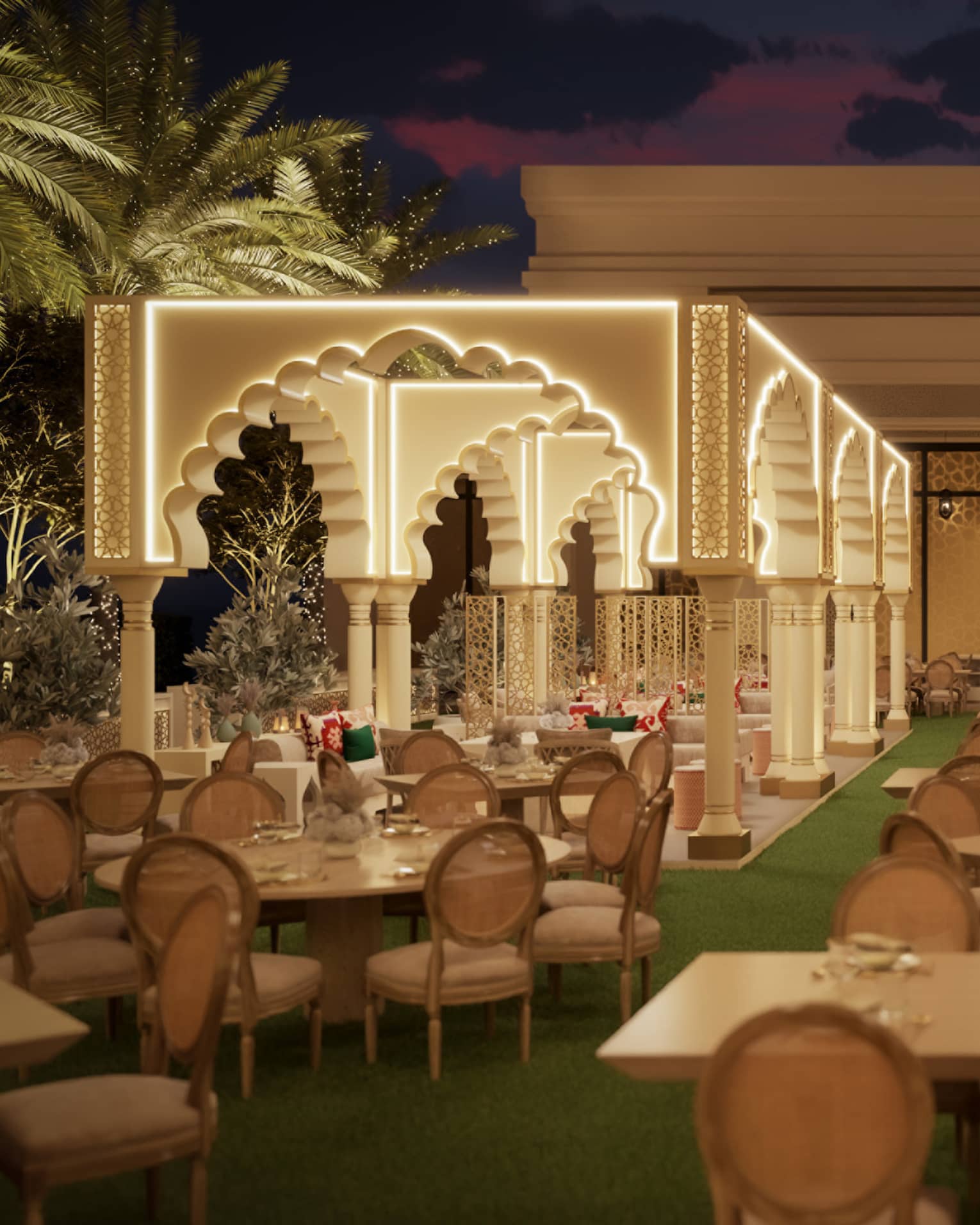 Outdoor lawn area filled with various white-topped tables with two rows of tall Arabesque archways lit up along the edges with palm trees seen along the perimeter, all beneath a night sky