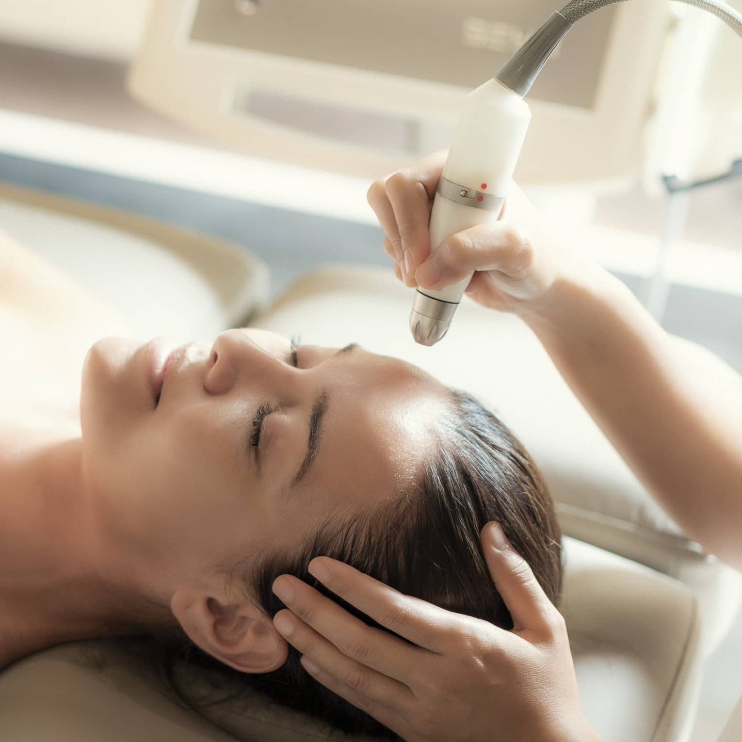 An aesthetician uses a tool on the face of a relaxing woman.