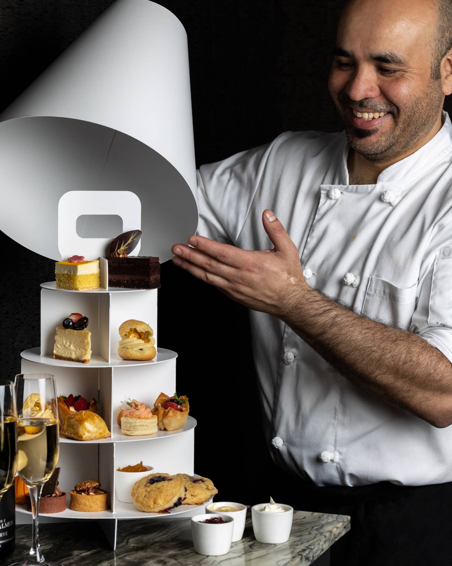 A chef revealing a three-tiered display of pastries and sweets.
