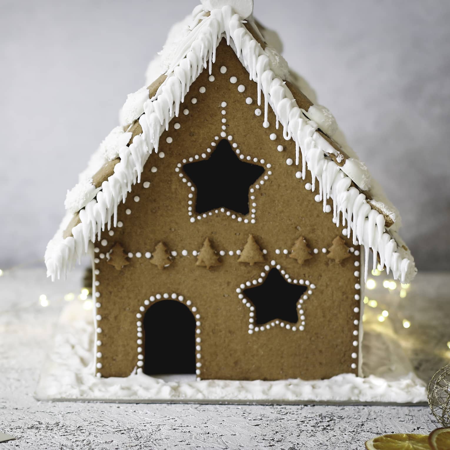 Gingerbread house decorated with white icing amid white background and white lights
