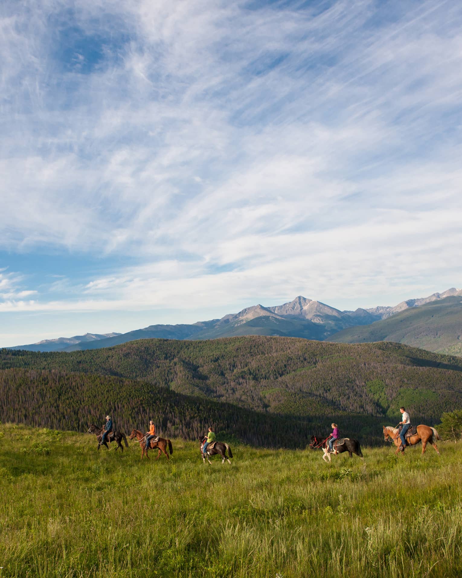 A group of people on horseback riding along grass and hills.