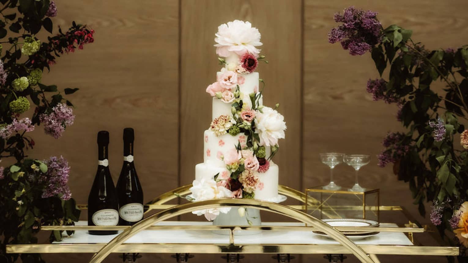 A platform with a tall cake, wine and wine glasses.