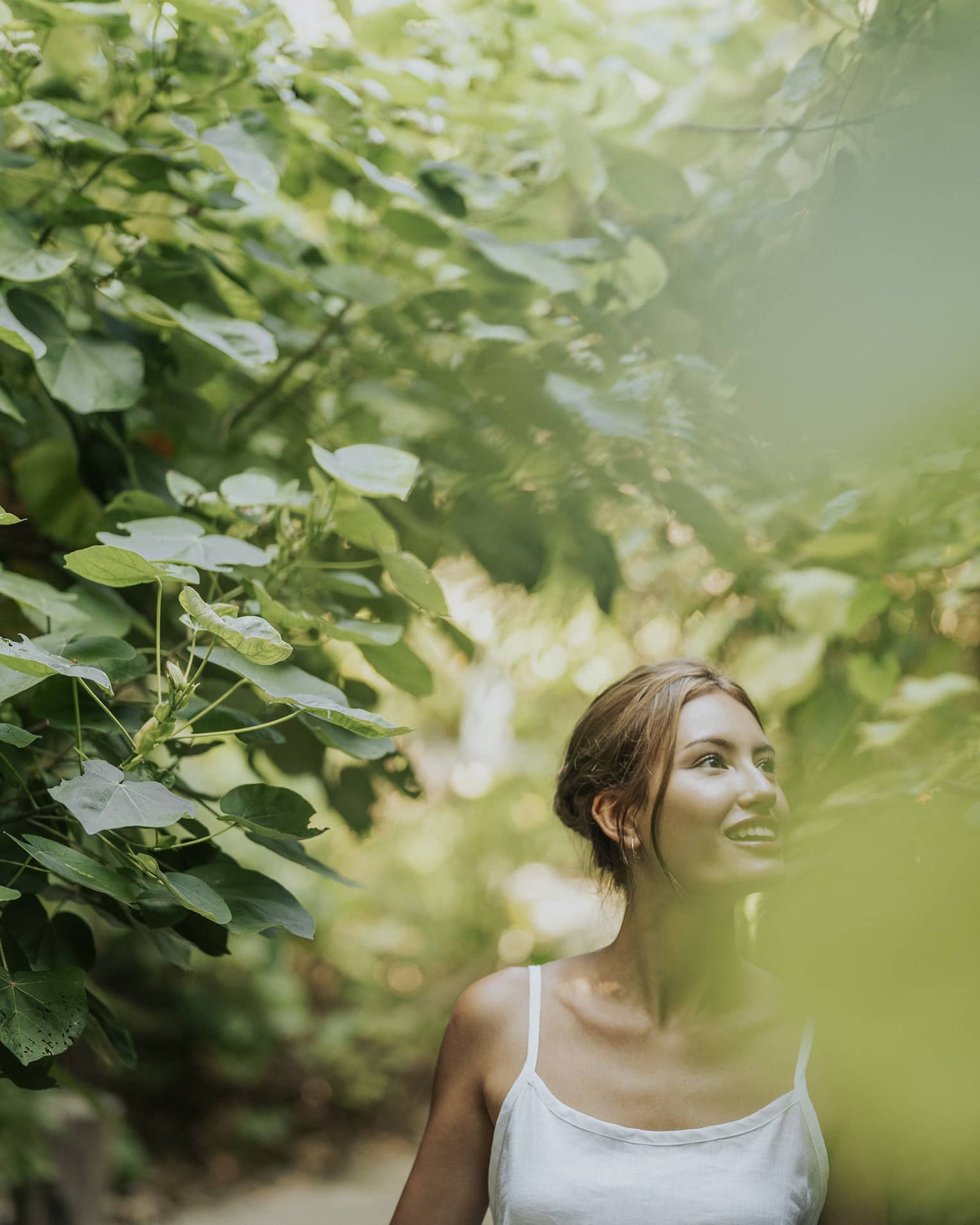 Woman in white tank top walks along heavily tree-lined path