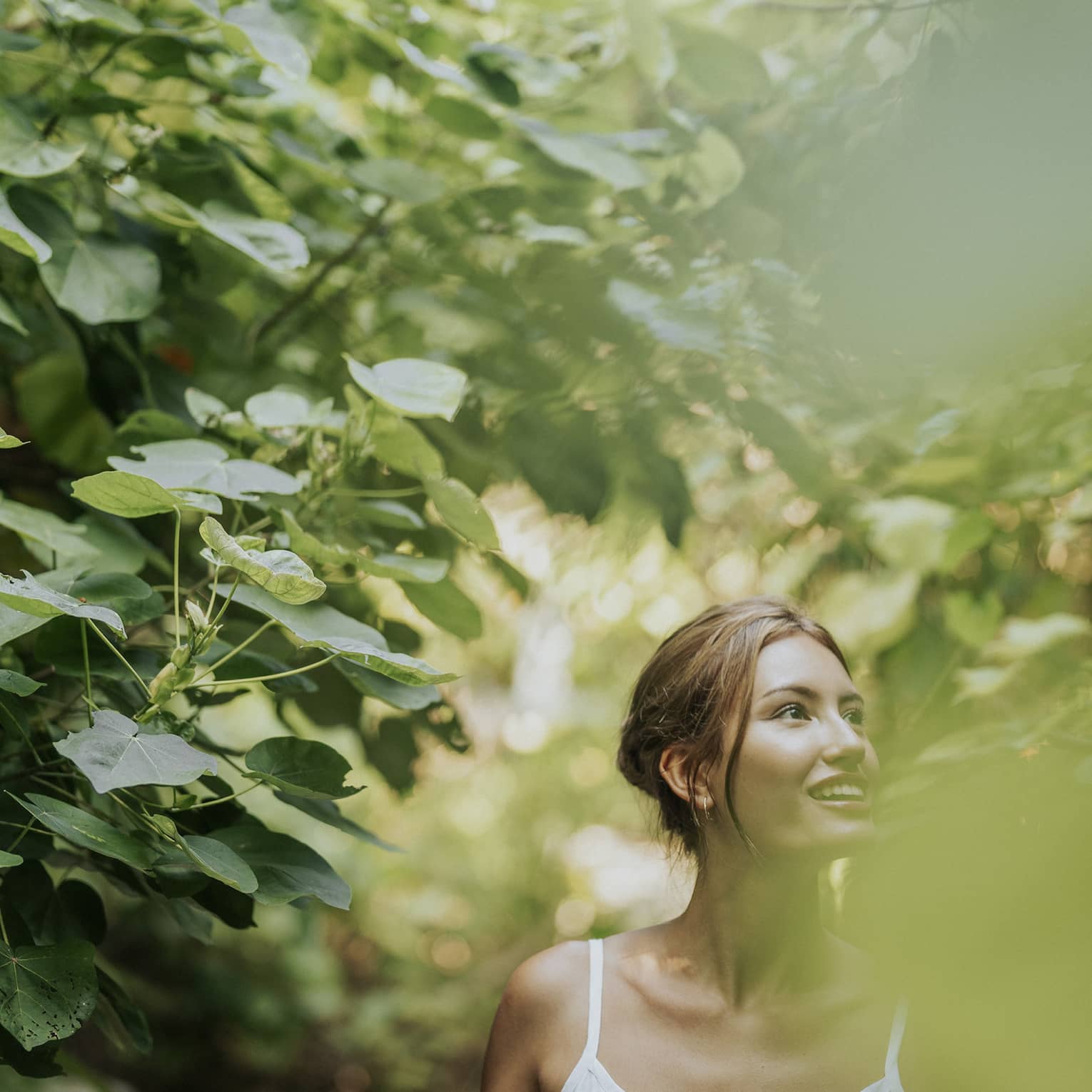Woman in white tank top walks along heavily tree-lined path