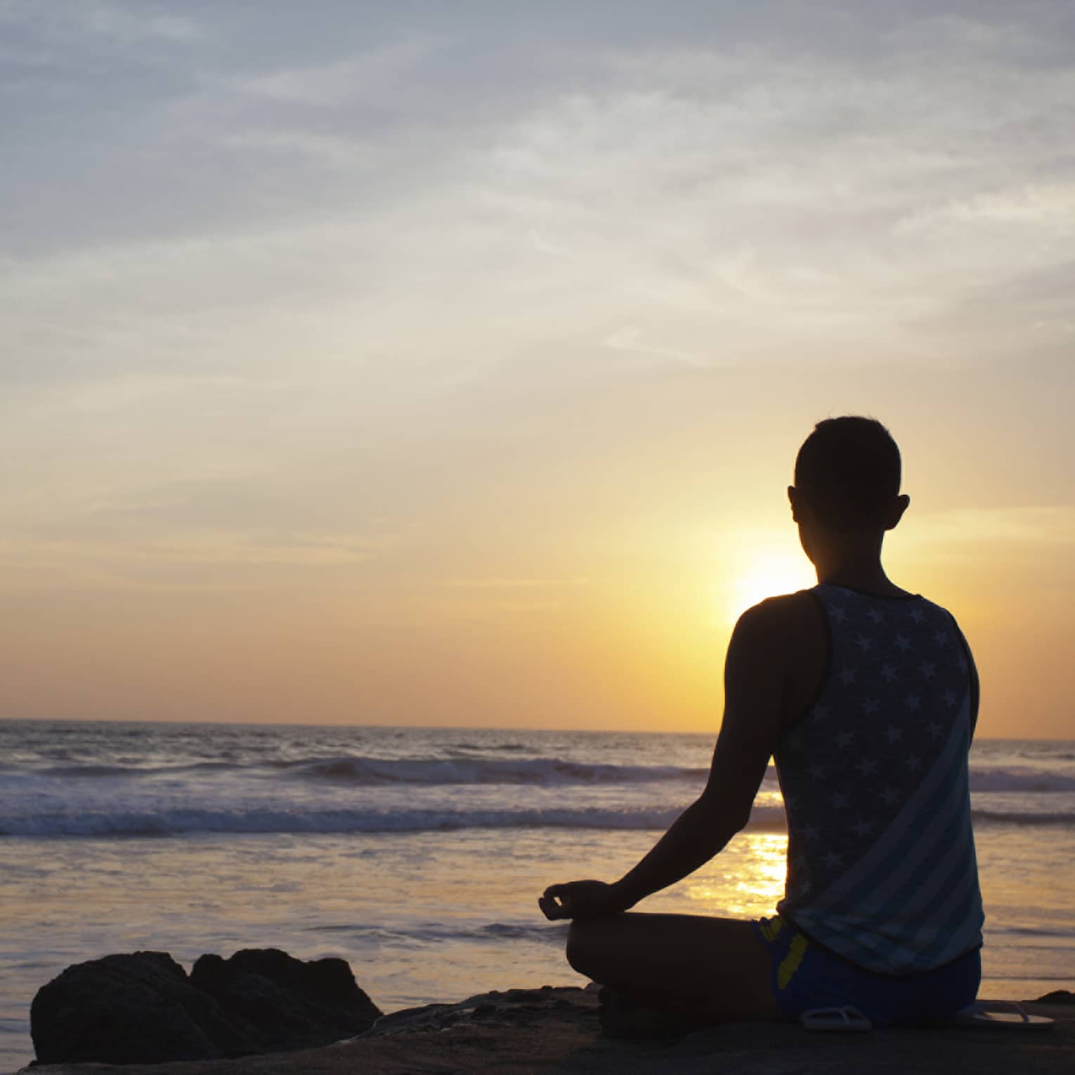 Silhouette of person sitting cross-legged, meditating in front of beach at sunset