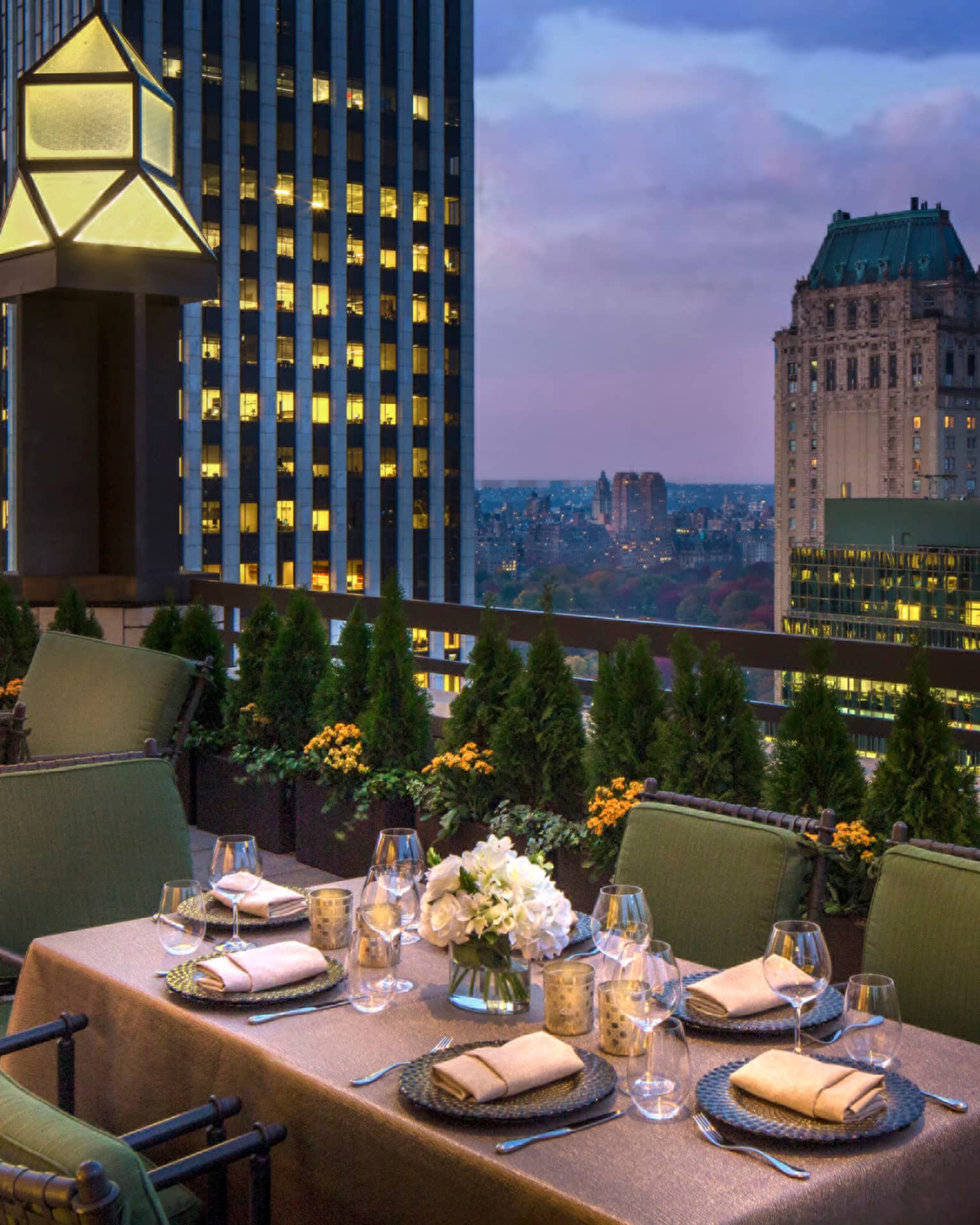 Private patio dining table with plush green cushions on chairs on rooftop terrace, city views at dusk