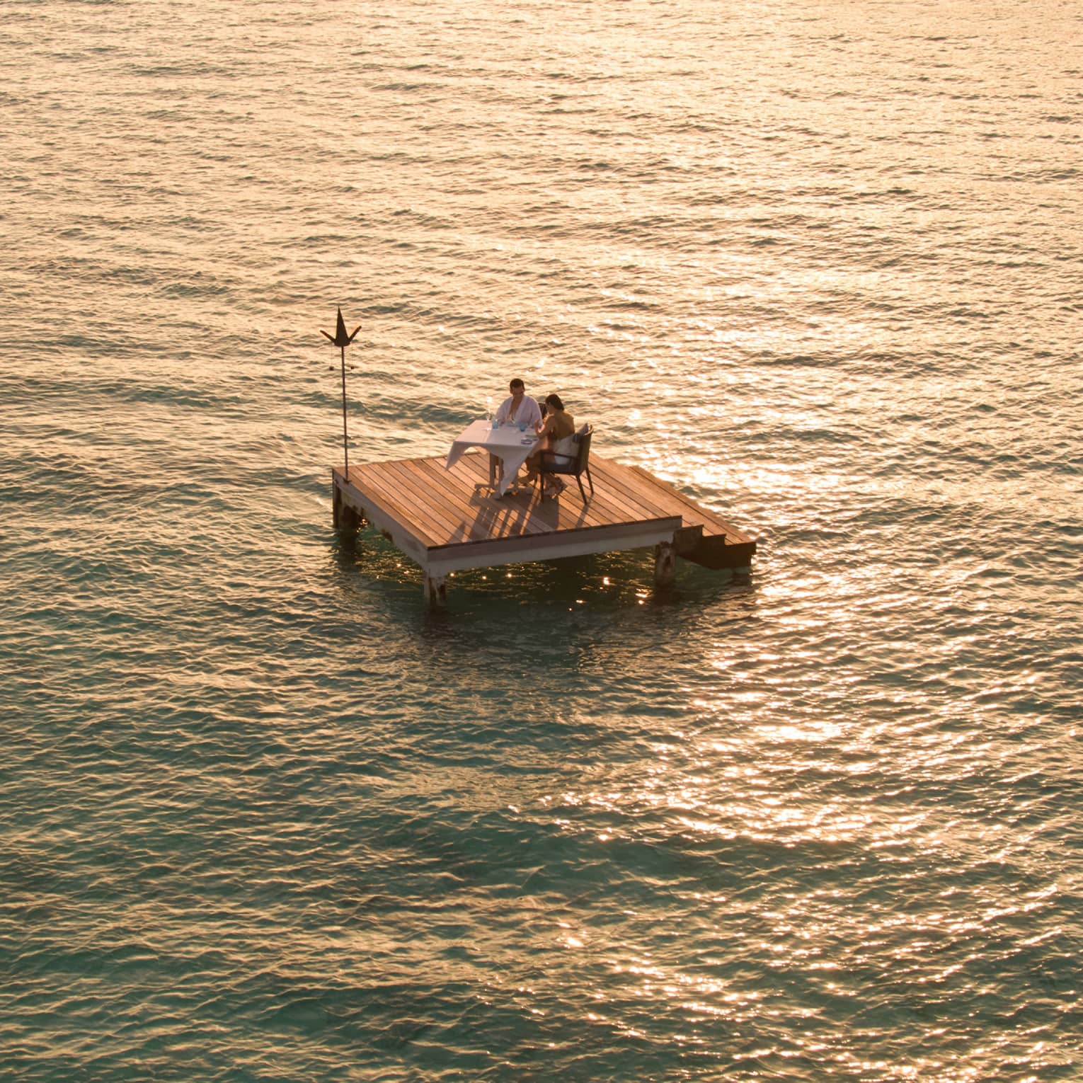 Aerial view of couple dining on small floating wood platform on moonlit lagoon