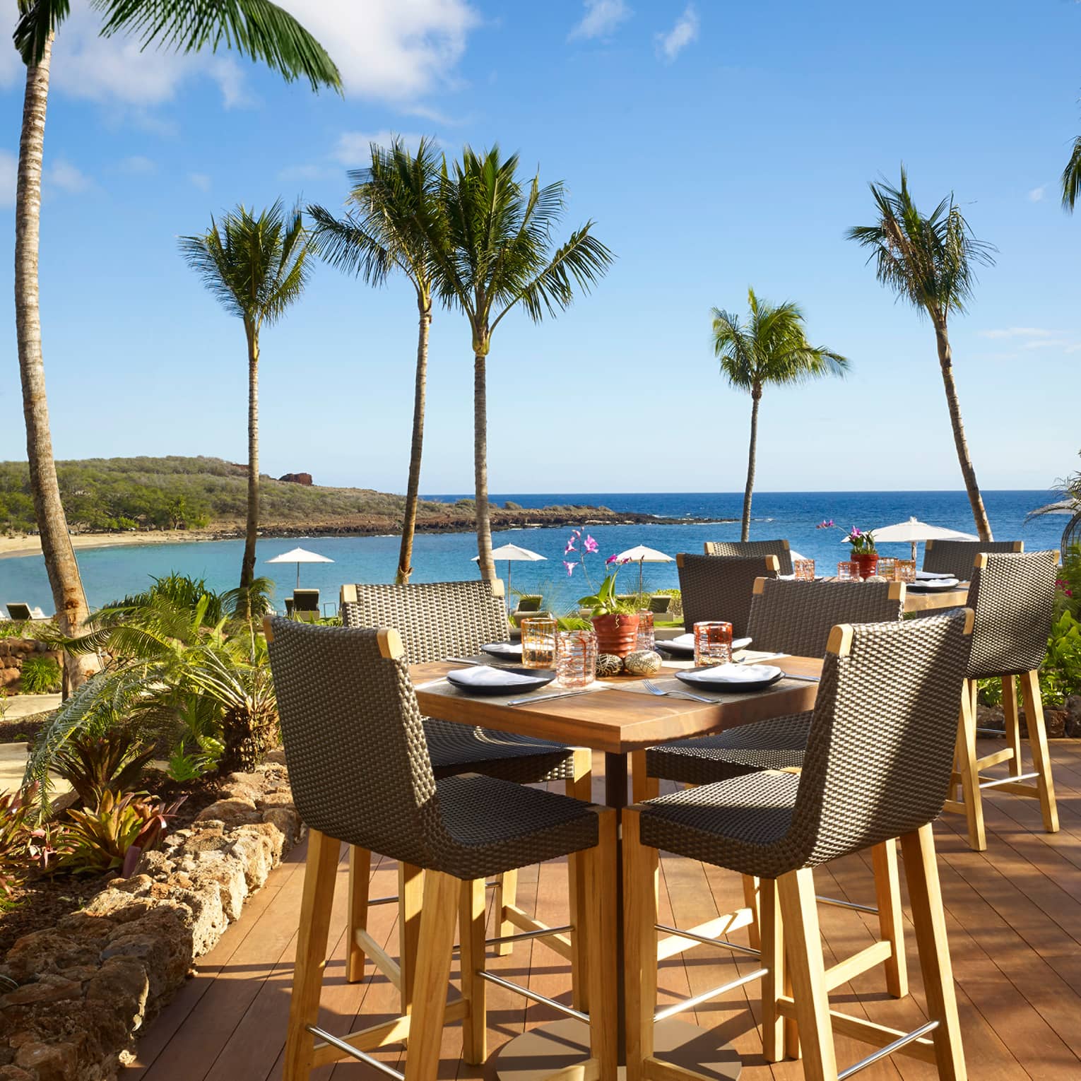 Malibu Farm Bar dining table, chairs on sunny patio overlooking beach, ocean
