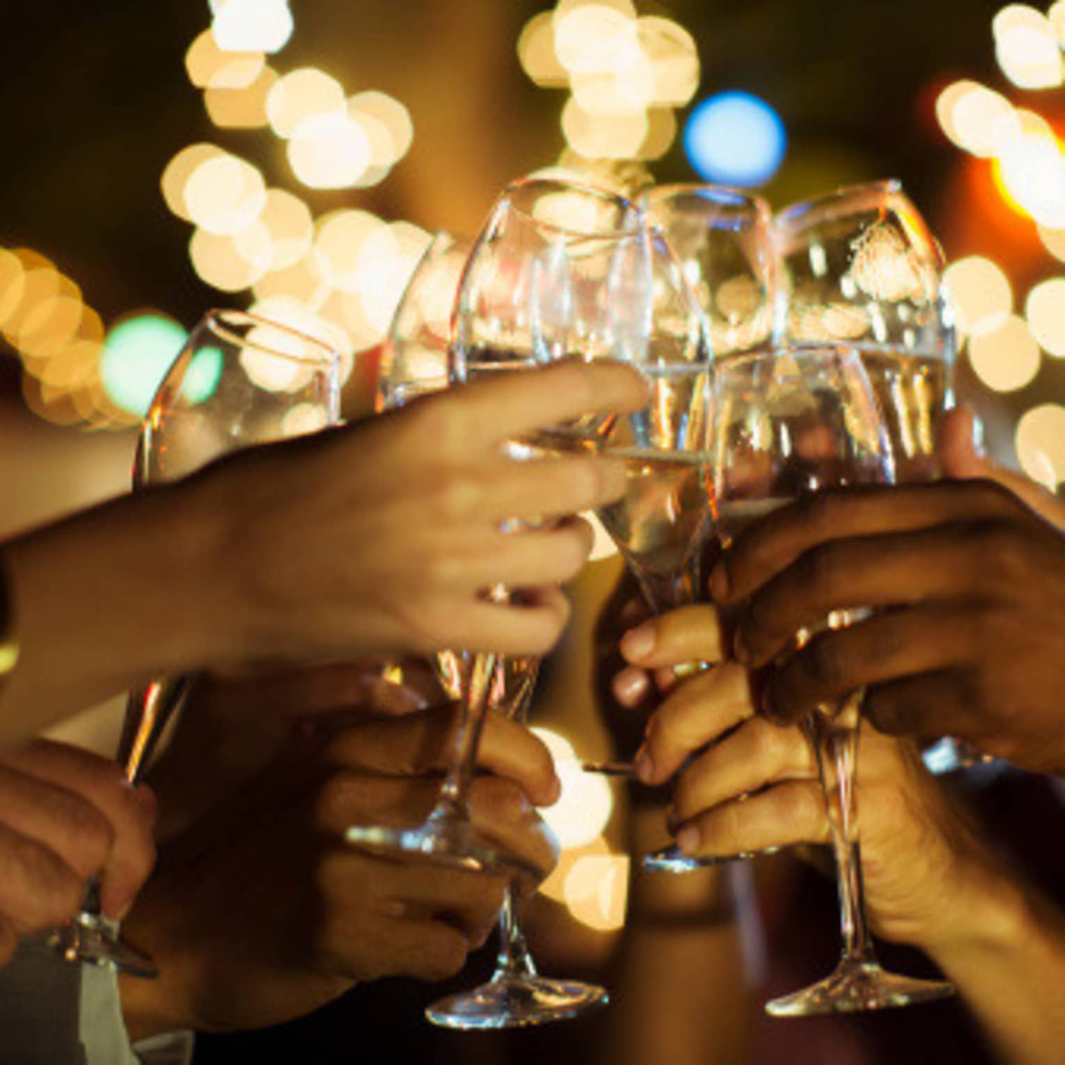 A group of guests clink their glasses of champagne together on a patio with twinkle lights
