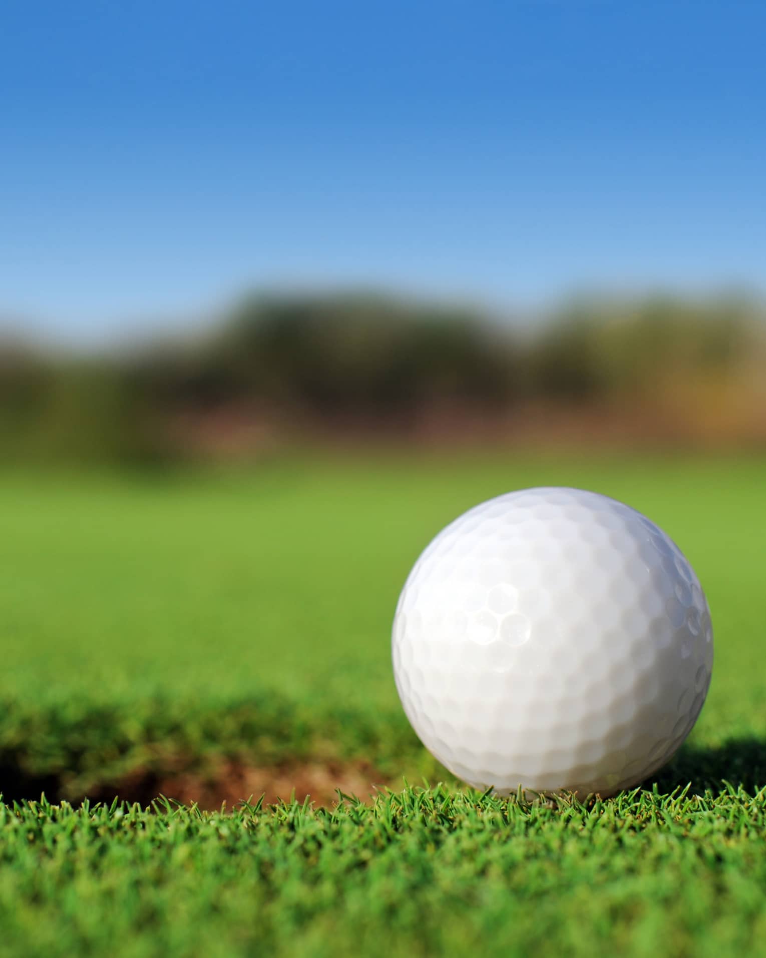 A close up of a white golf ball sitting right next to a golf hole on the course