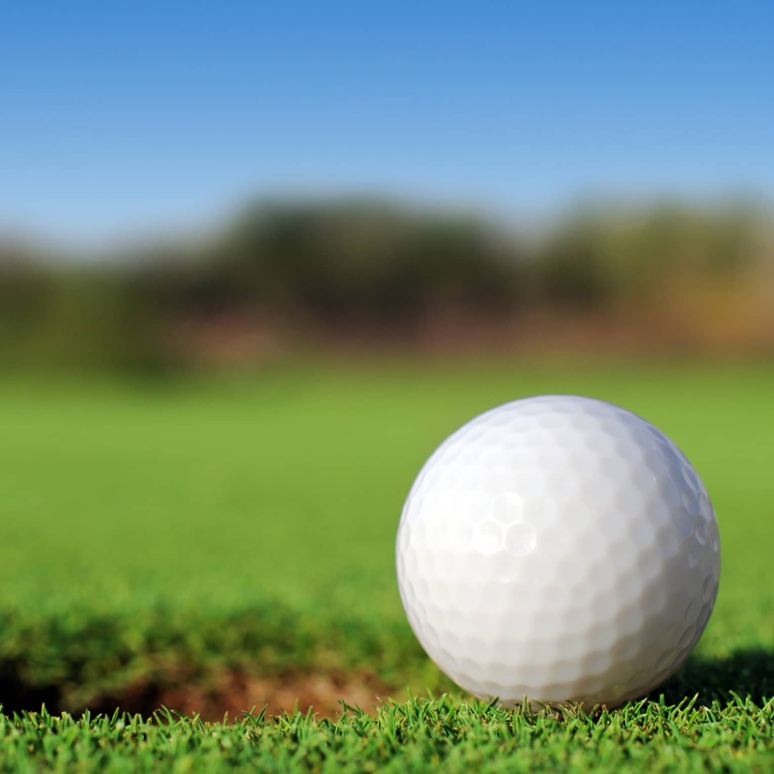 A close up of a white golf ball sitting right next to a golf hole on the course