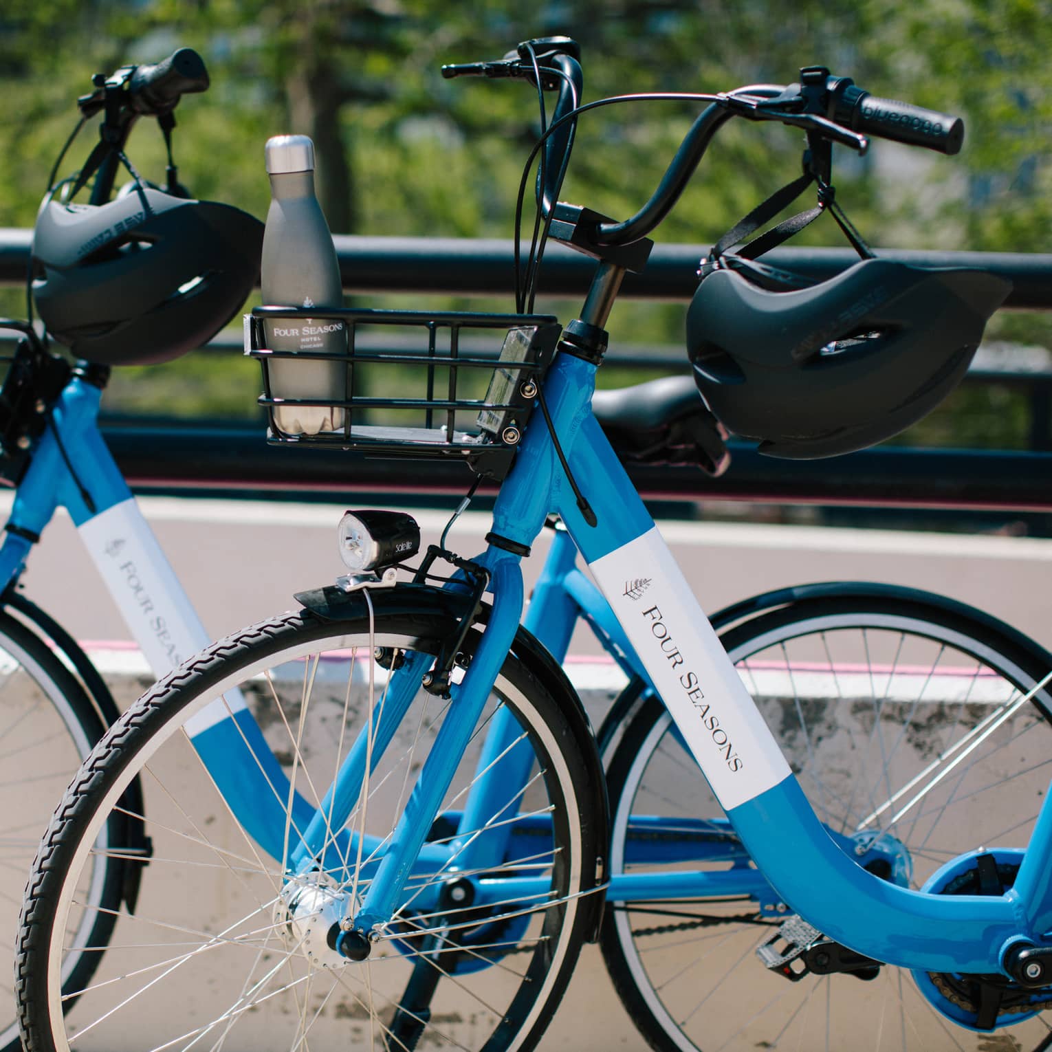 Close-up of two blue Four Seasons bicycles with helmets hanging on the handlebars and a water bottle in one bicycle's basket.
