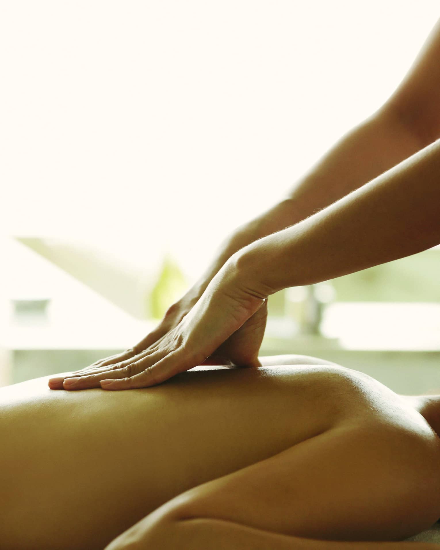 Masseuse reaches over, massages woman's bare back as she lies on spa table