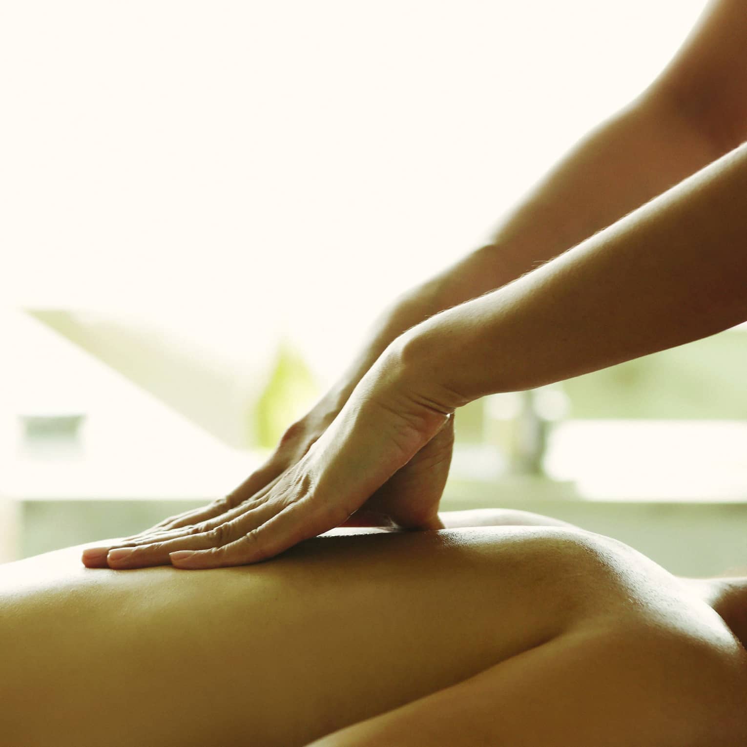 Masseuse reaches over, massages woman's bare back as she lies on spa table